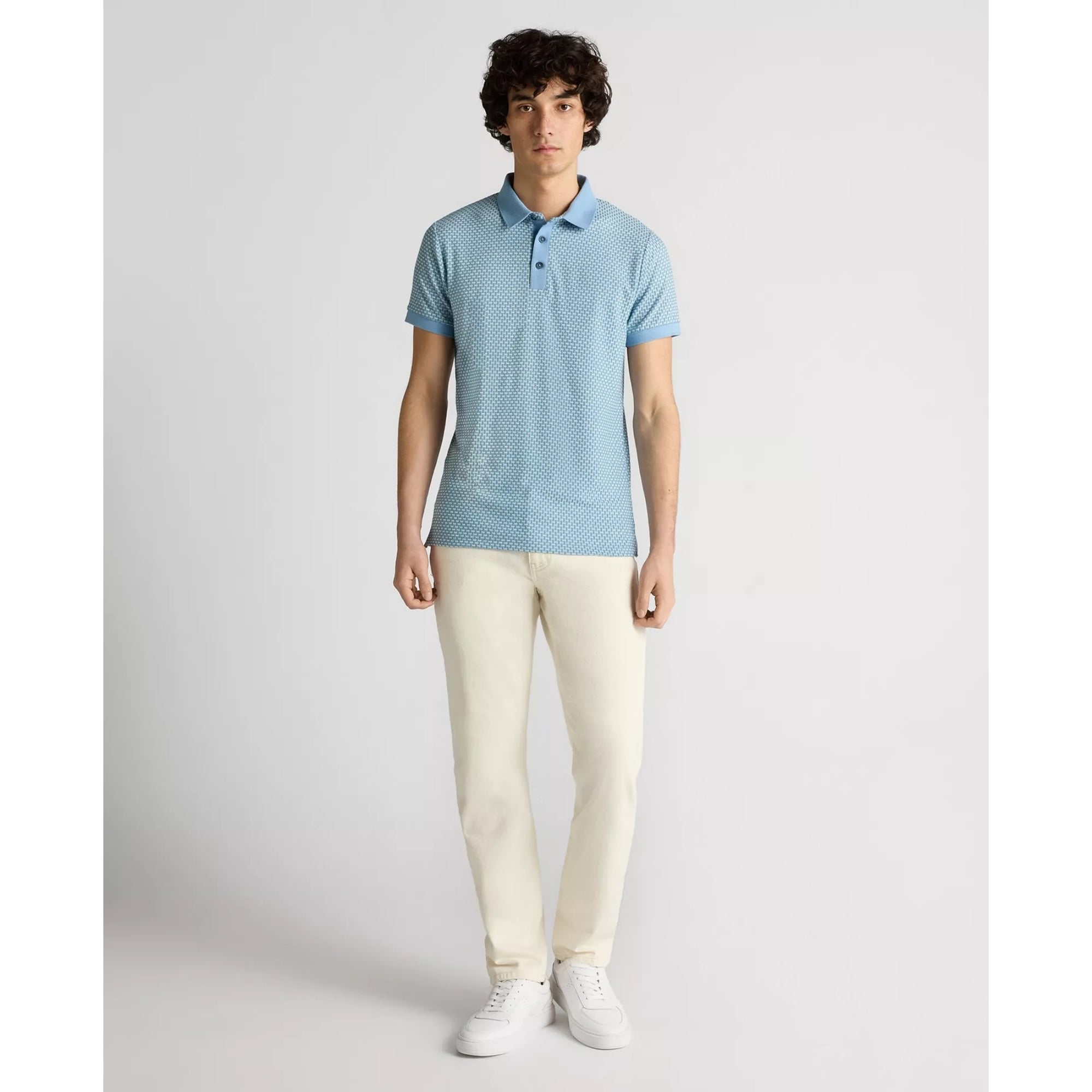 Man wearing a light blue polo shirt and white pants on a plain background