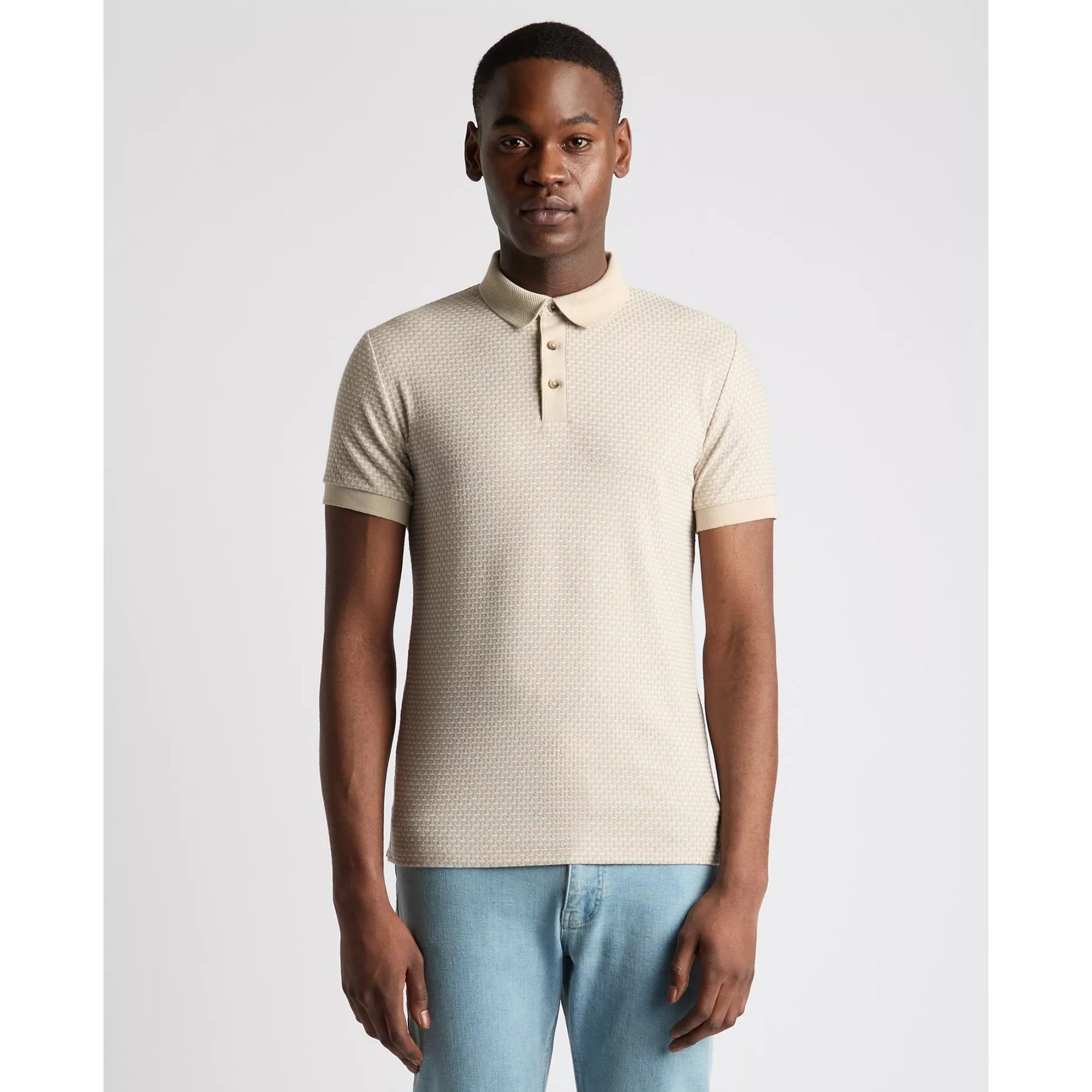 Man wearing a beige patterned polo shirt and light blue jeans on a white background