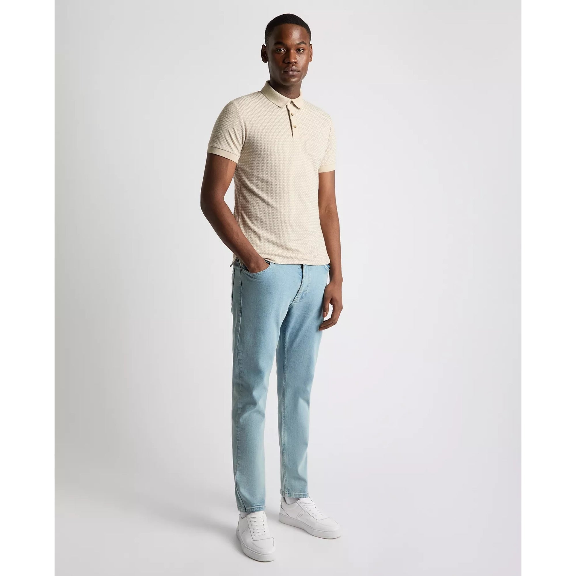 Man wearing a beige polo shirt and light blue jeans on a white background