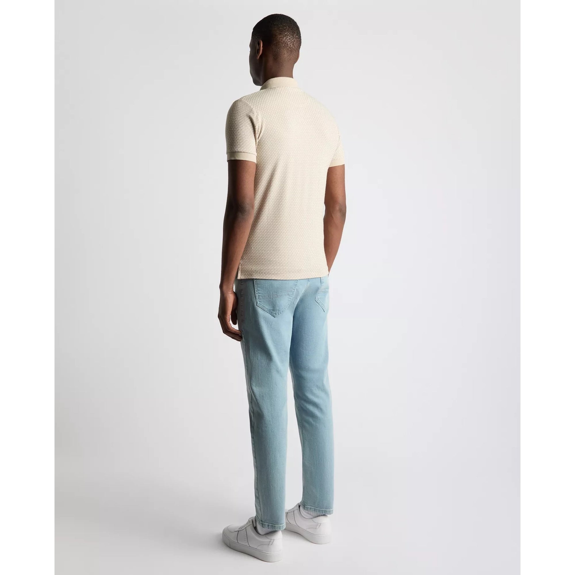 Person wearing a beige polo shirt and light blue jeans on a white background