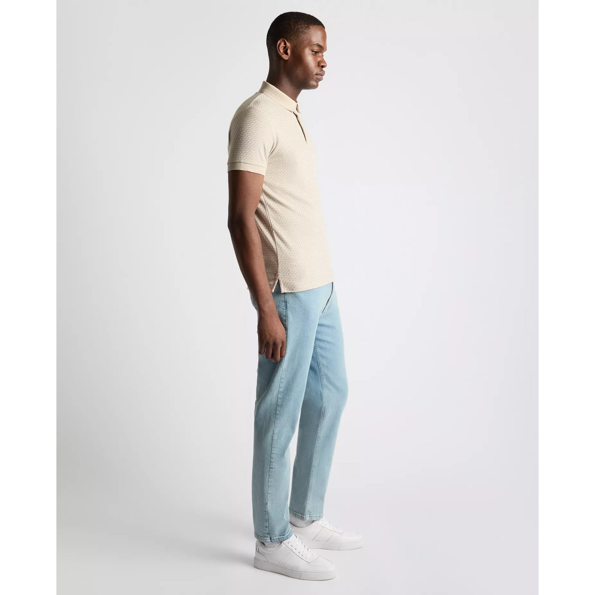 Man wearing a beige shirt and light blue pants on a white background