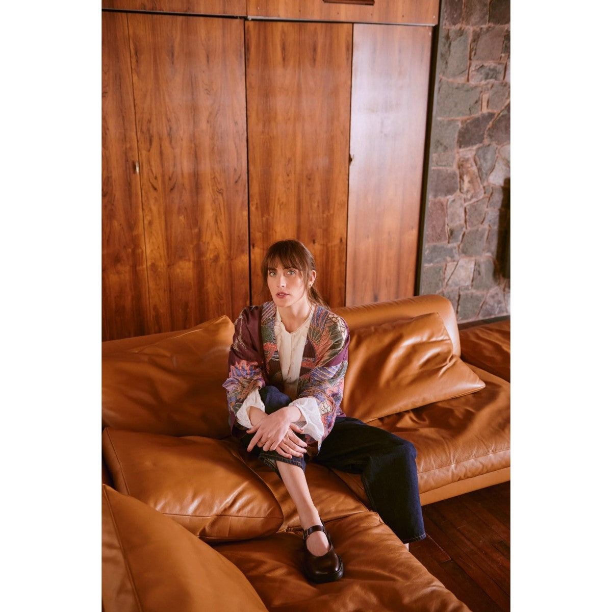 Person sitting on a brown leather couch in a room with wooden walls and a stone wall.