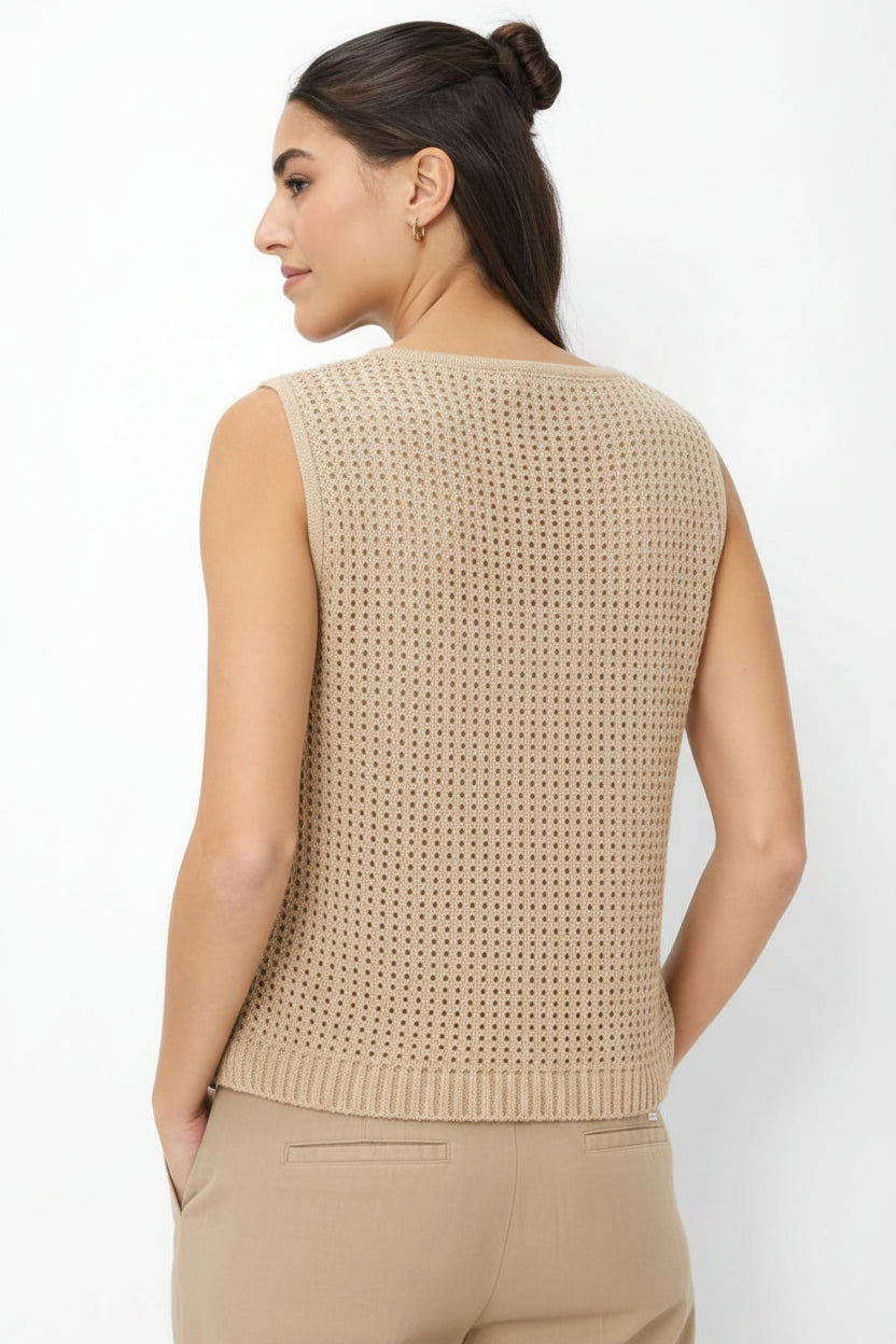 Woman wearing a beige sleeveless knitted top against a white background