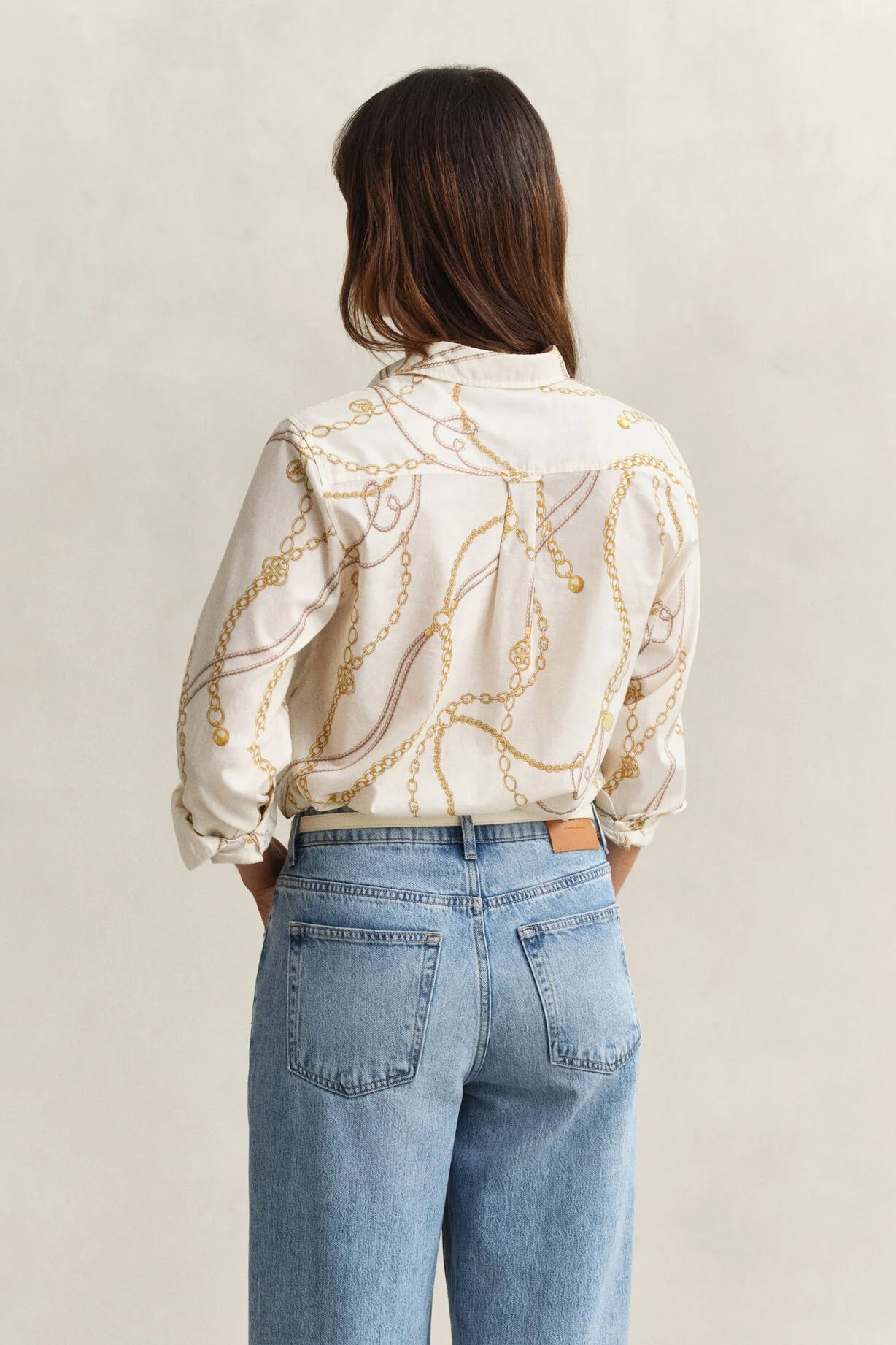 Person wearing a patterned blouse and blue jeans against a plain background