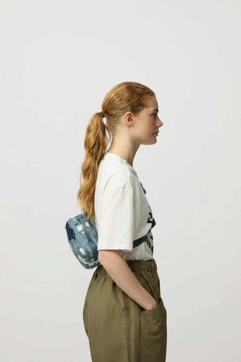Woman wearing a white t-shirt with text and a blue patterned backpack on a light gray background