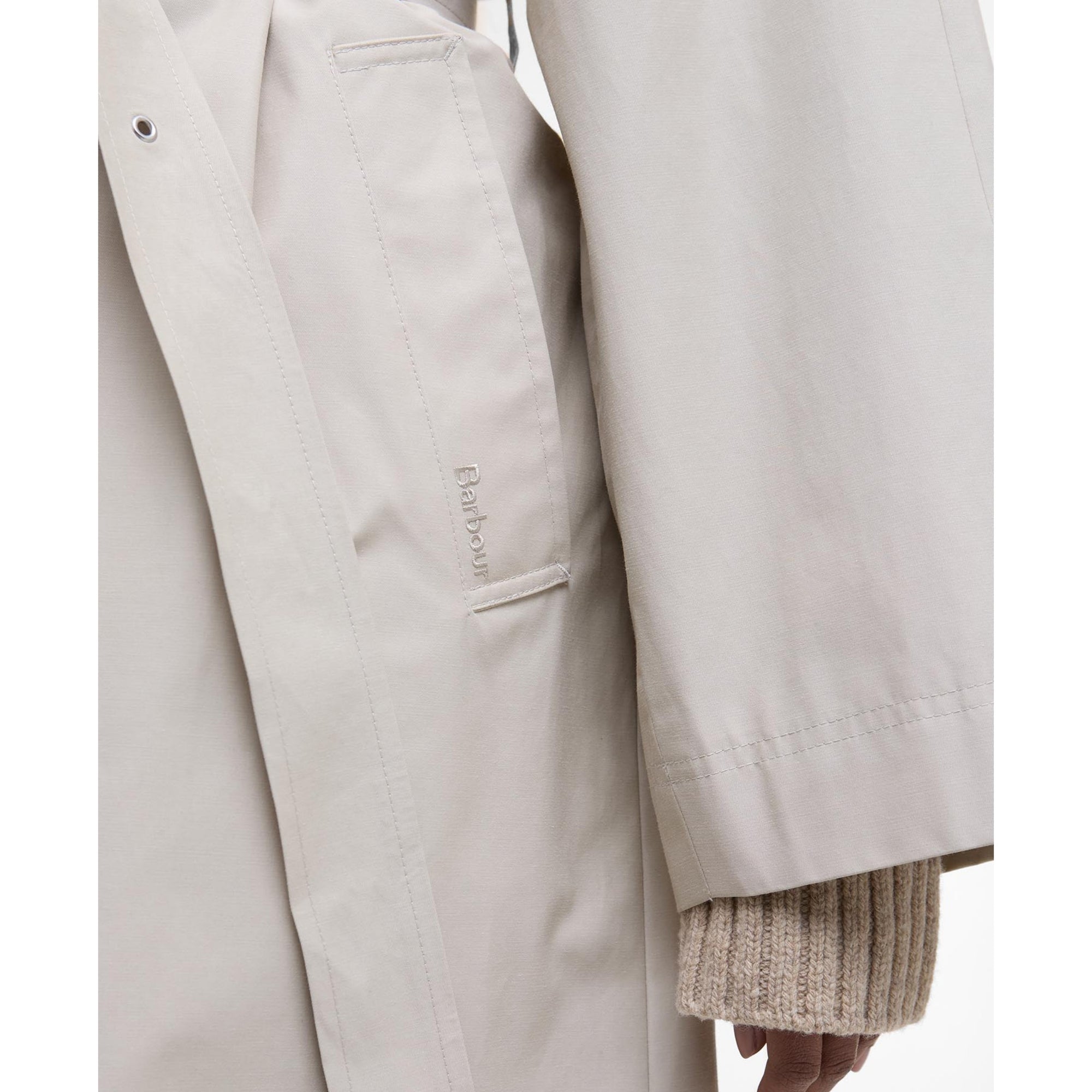 Close-up of a beige trench coat with a brand logo on a white background