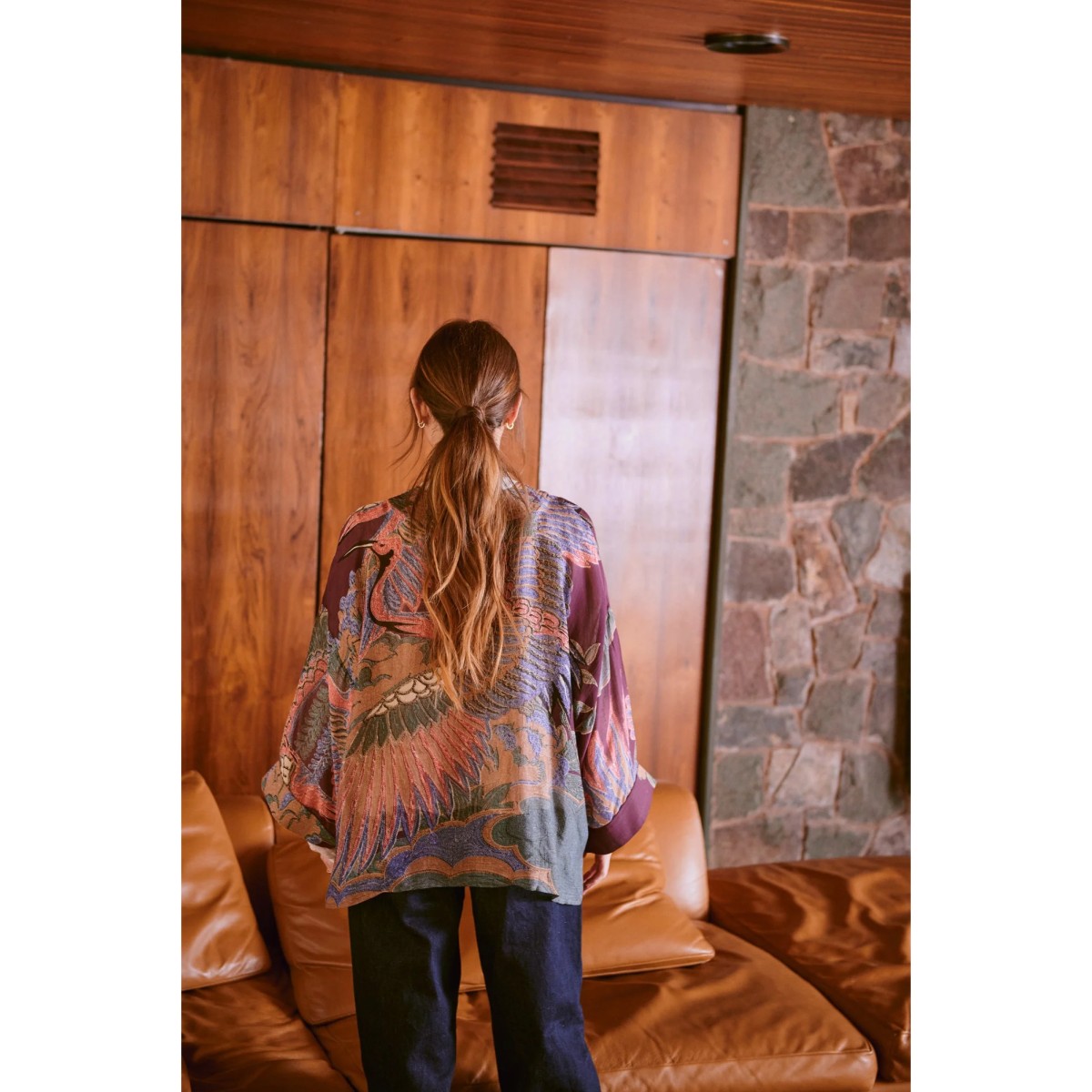 Person wearing a patterned kimono standing in a room with wooden walls and a stone wall.