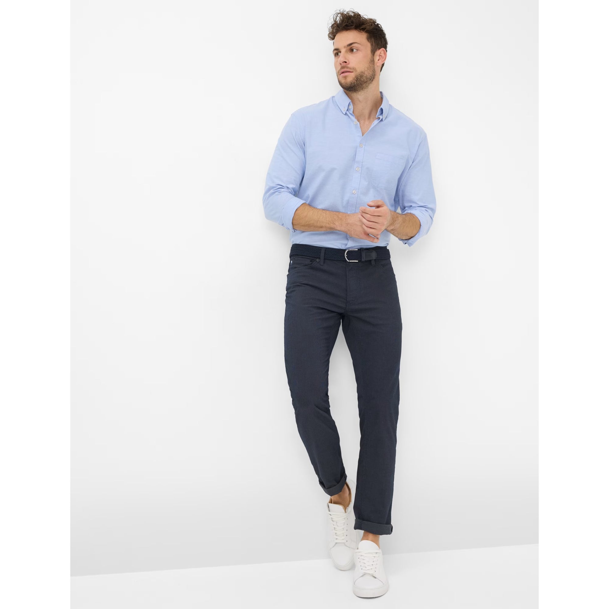 Man wearing a light blue shirt and dark pants on a white background