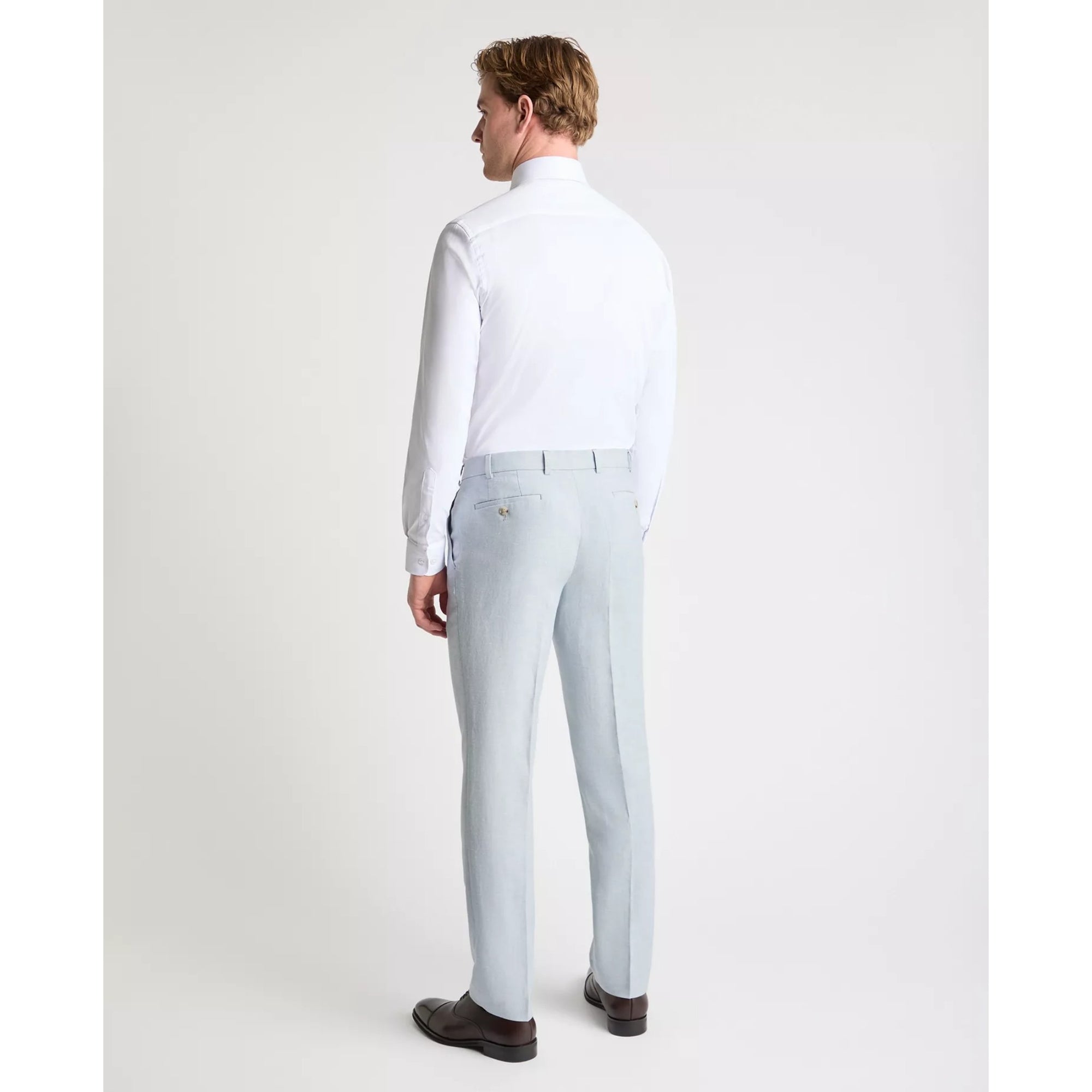 Man wearing a white dress shirt and light blue pants on a plain background