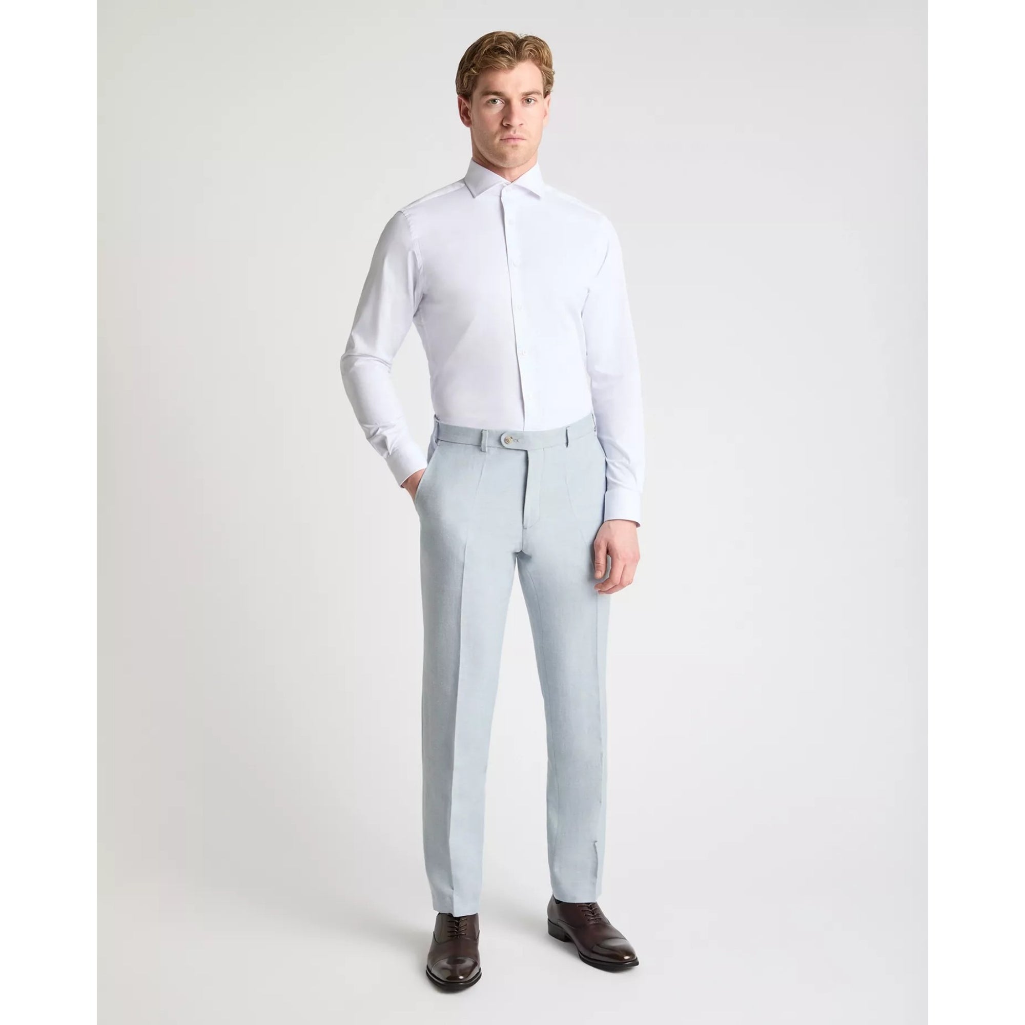 Man wearing a white dress shirt and light blue pants on a plain background