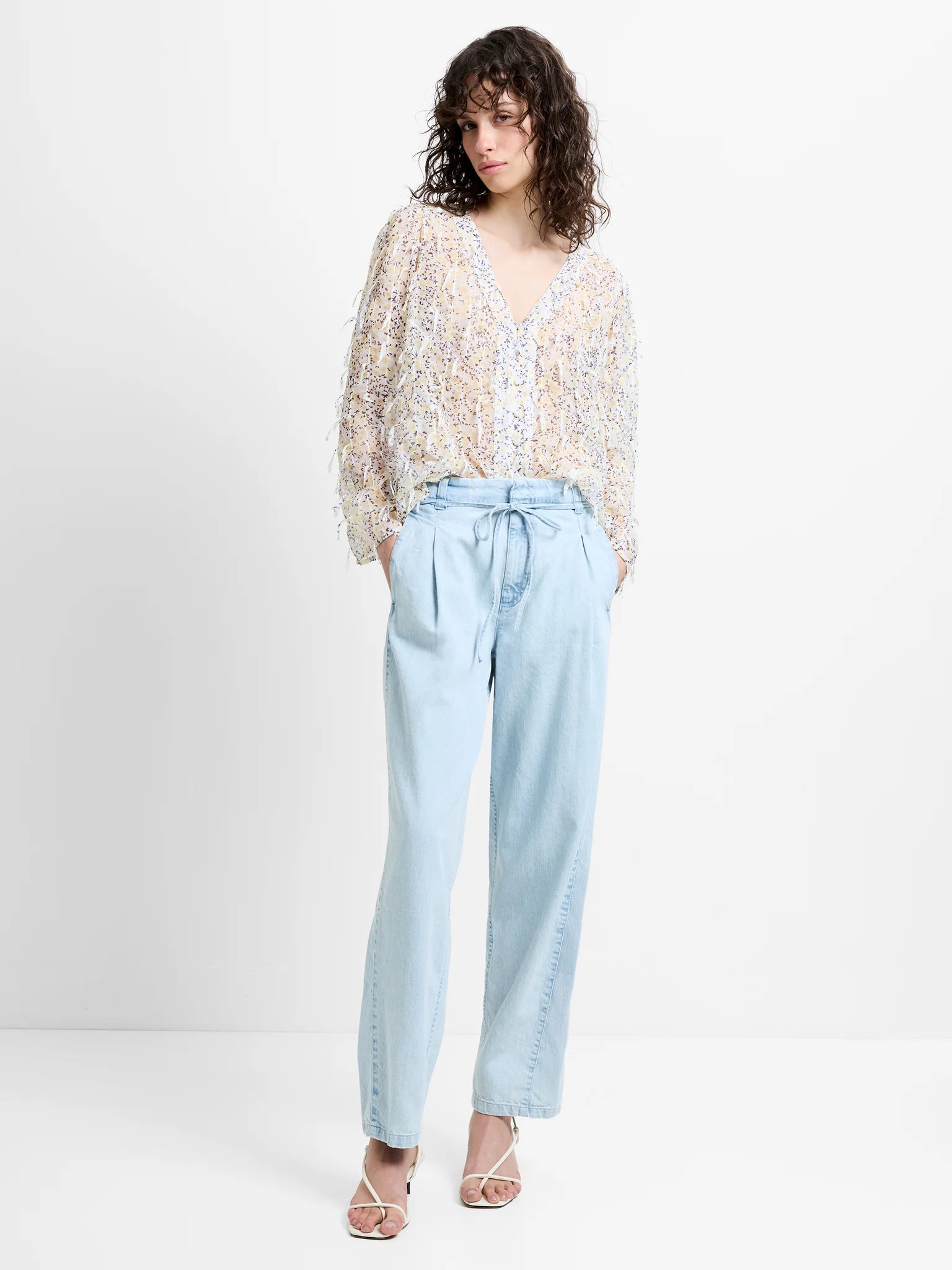 Woman wearing a patterned top and light blue pants on a white background