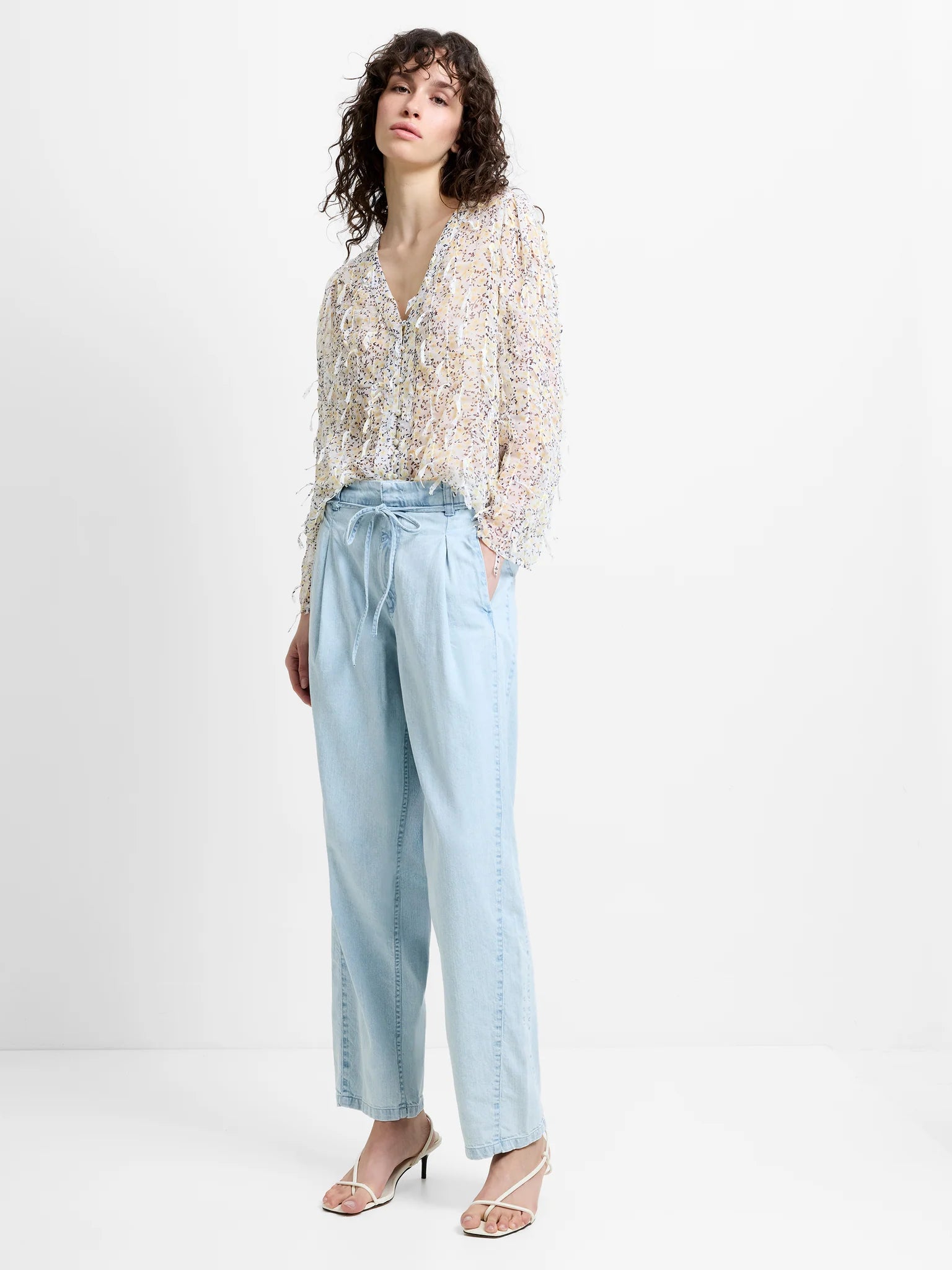 Woman wearing a floral blouse and light blue jeans on a white background