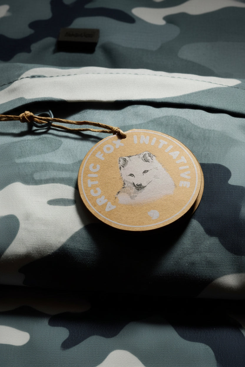 Round cardboard tag with Arctic Fox Initiative logo on a camouflage fabric background