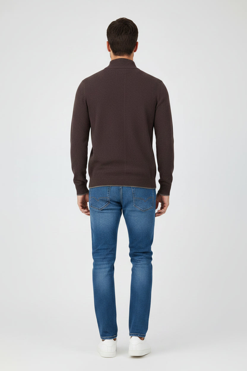 A man modeling a dark brown quarter-zip knit sweater with blue jeans and white sneakers, standing against a light gray studio background.