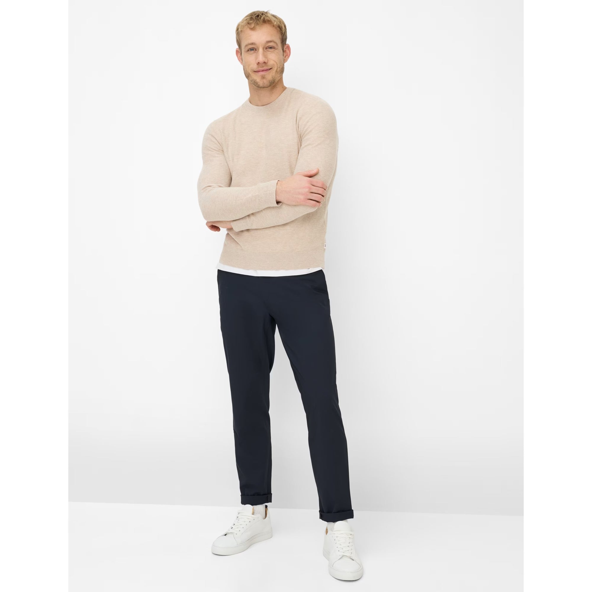 Man wearing a beige sweater and navy pants with white shoes on a white background