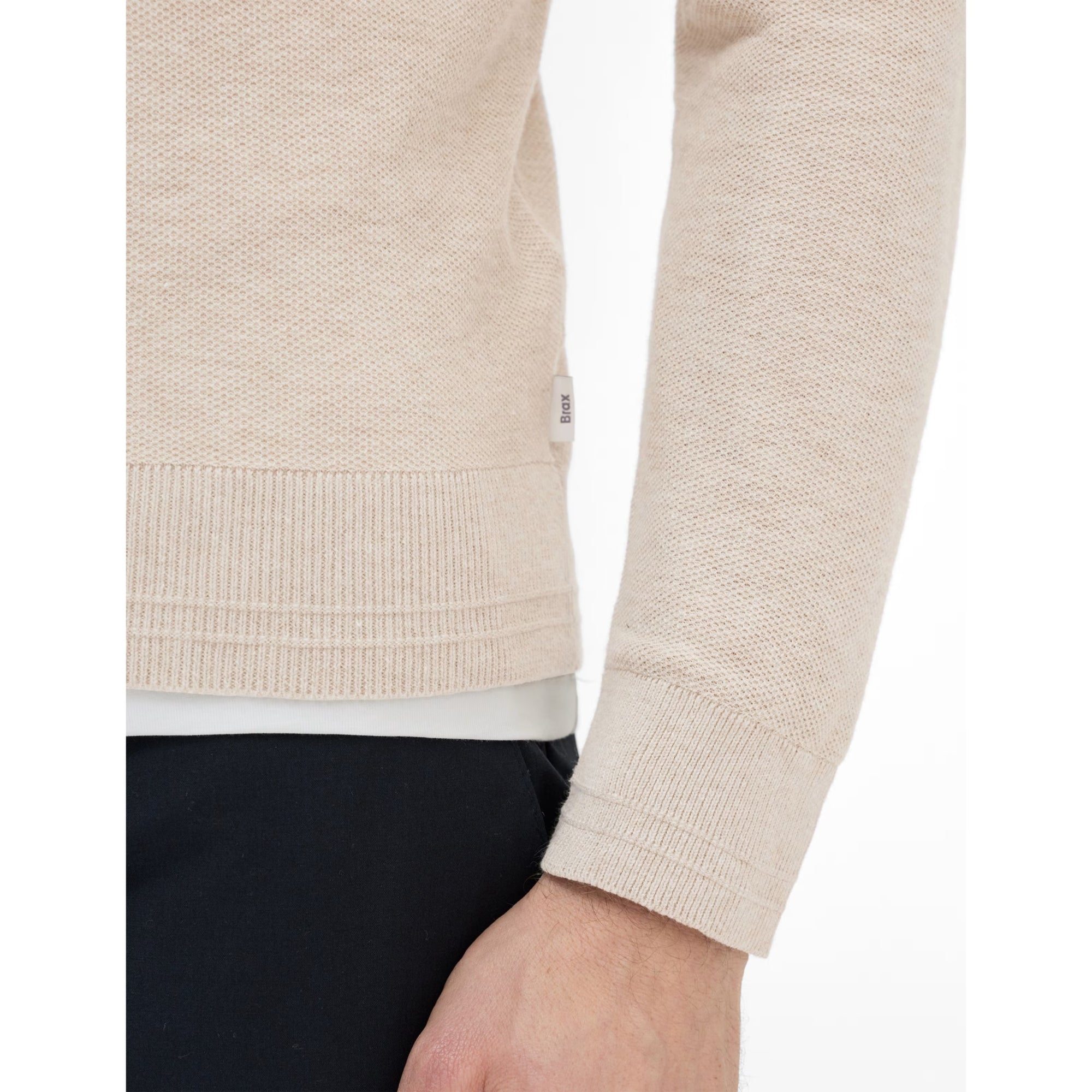 Close-up of a beige sweater with a brand logo on a white background