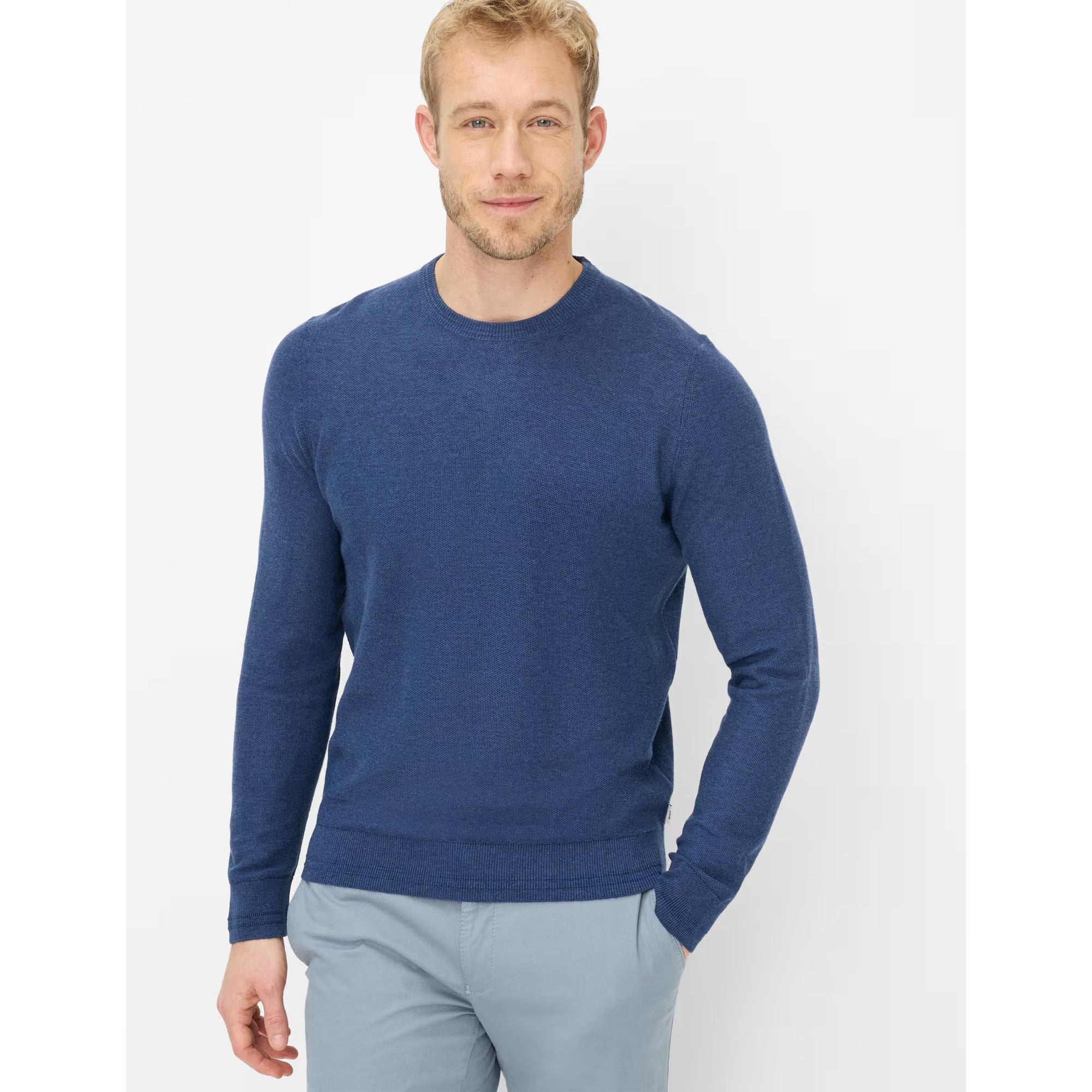 Man wearing a blue sweater and light gray pants on a white background