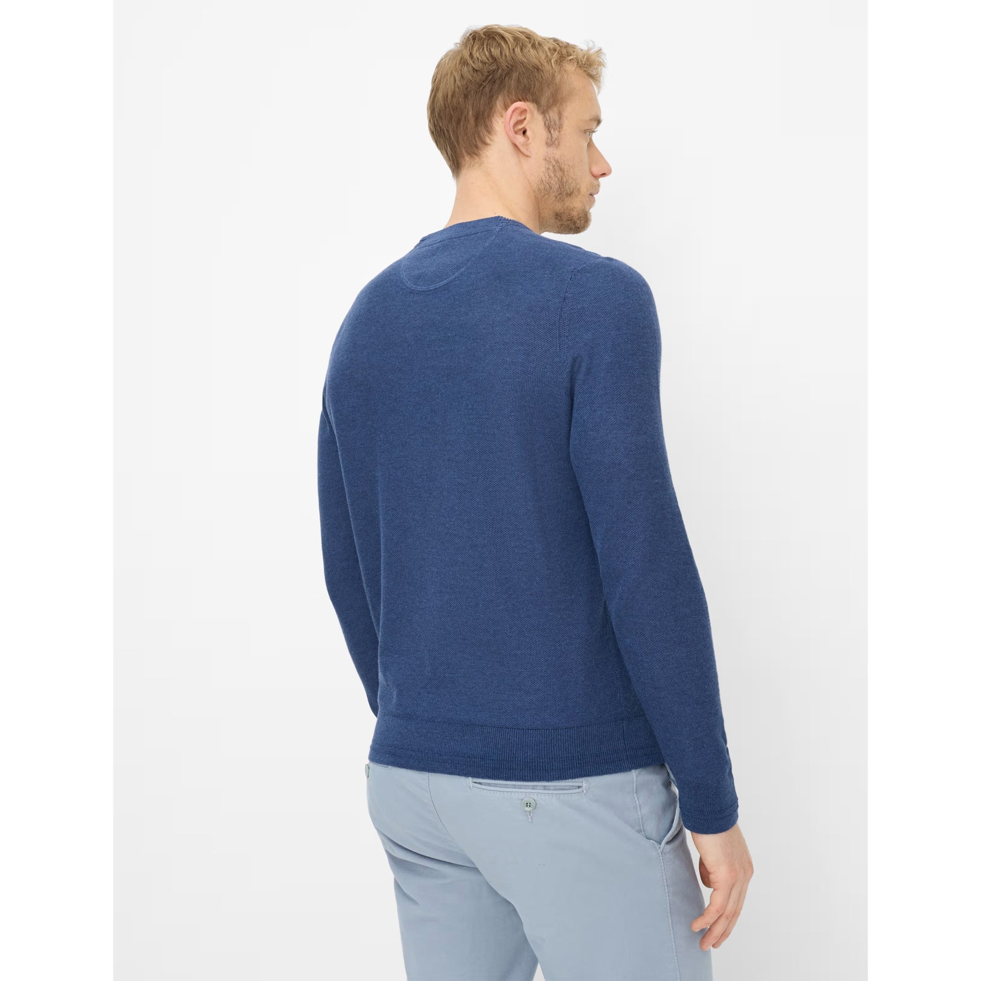Man wearing a blue sweater and light blue pants on a white background