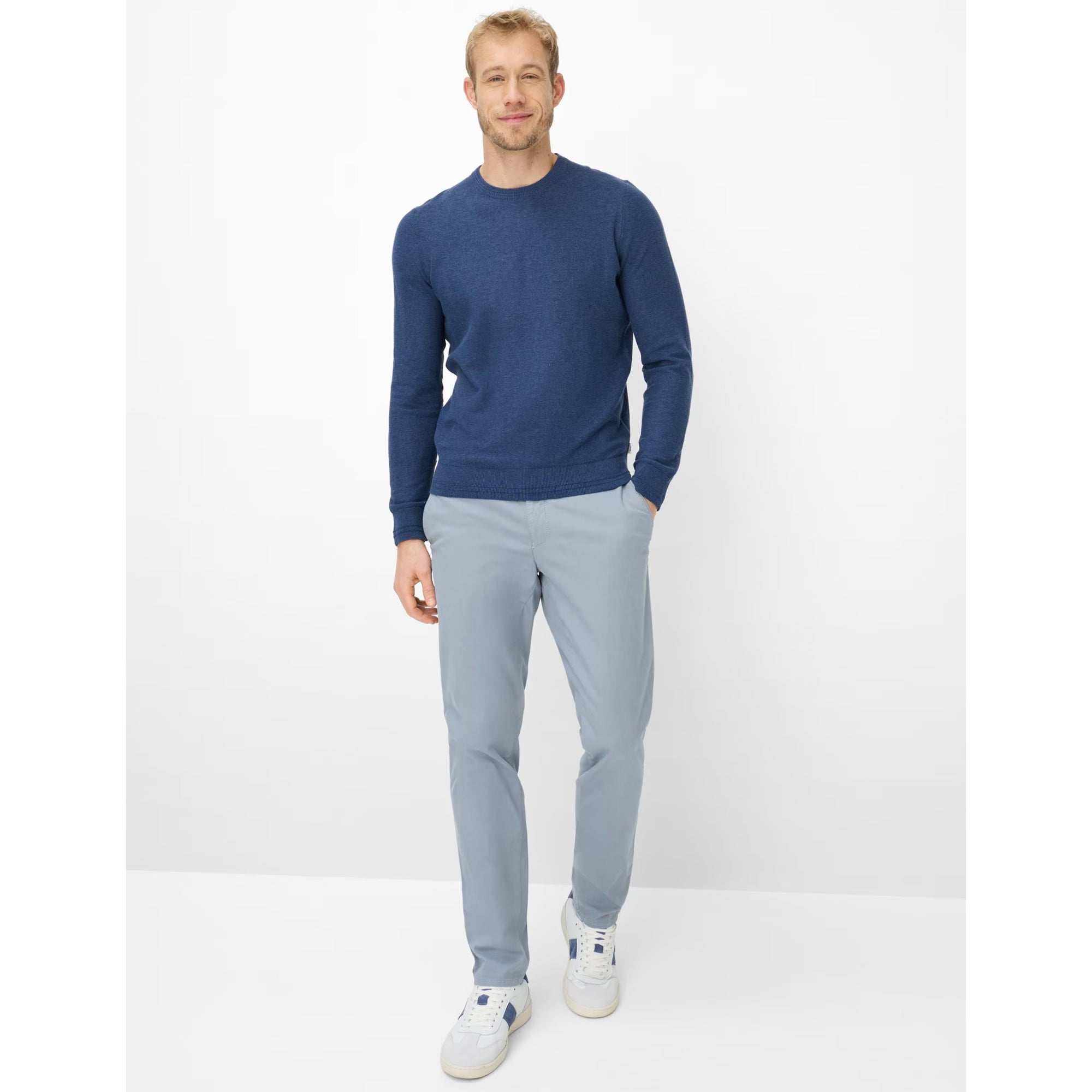 Man wearing a blue sweater and light gray pants on a white background