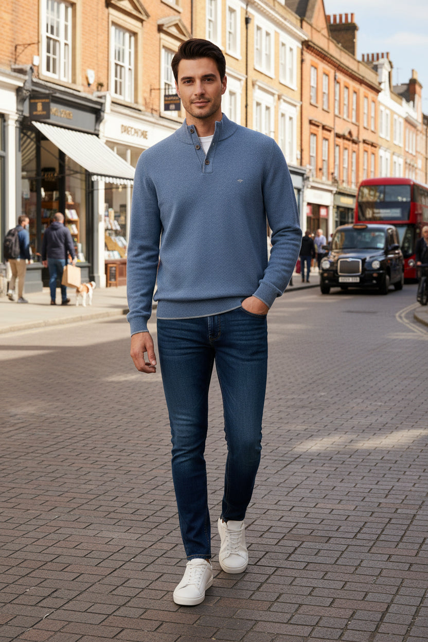 A man modeling a light blue quarter-zip knit sweater, dark blue jeans, and white sneakers.