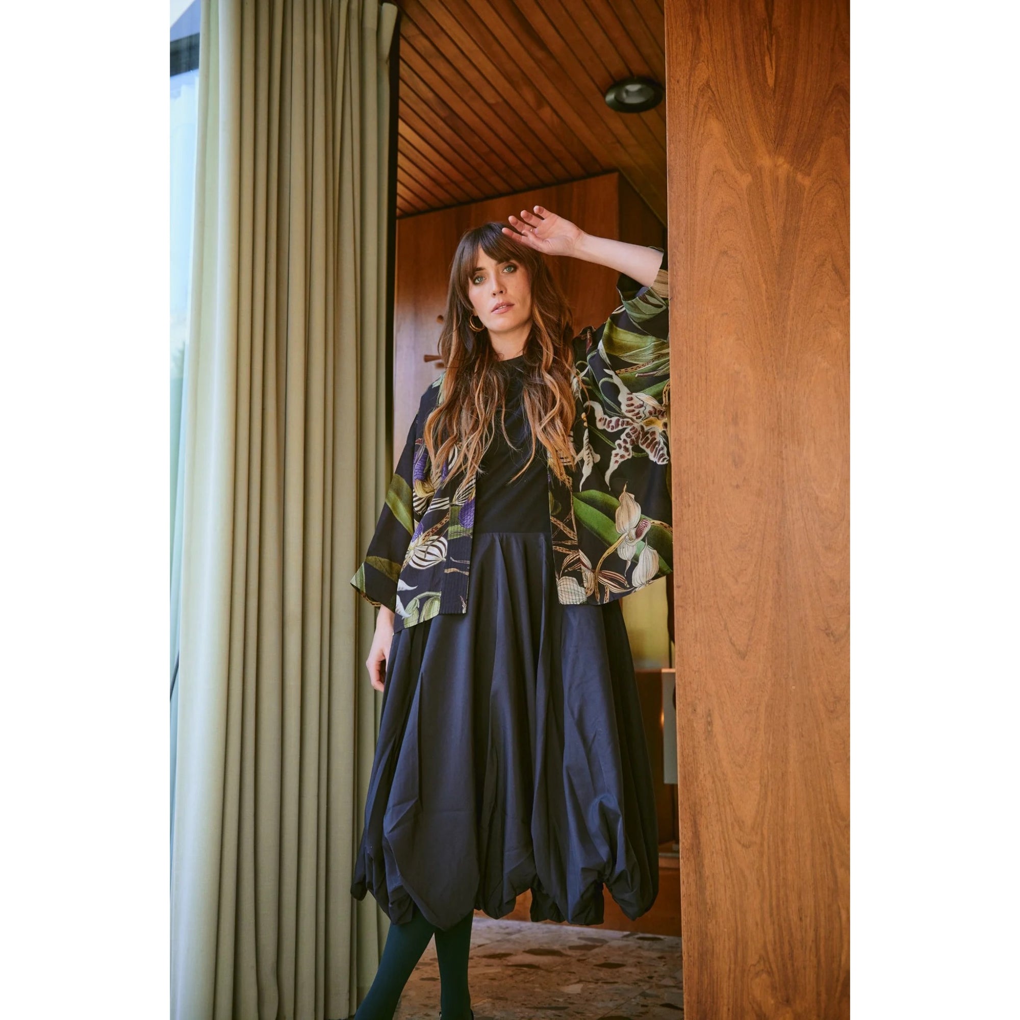 Woman standing in a doorway wearing a floral kimono and dark dress.