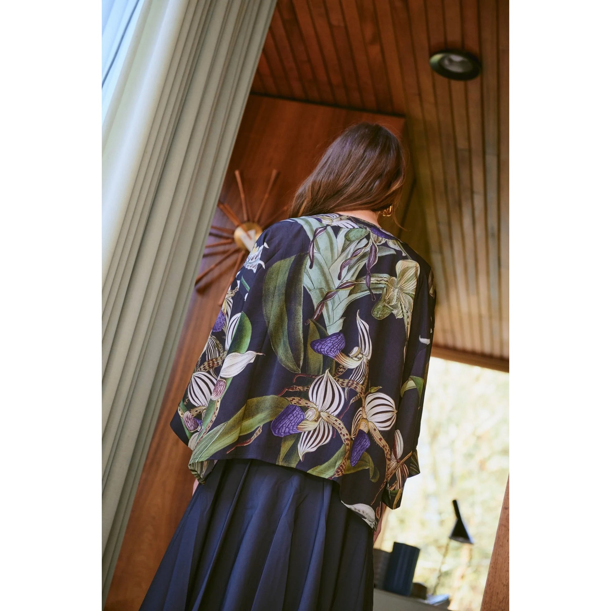 Woman wearing a floral-patterned top and dark skirt in an indoor setting.