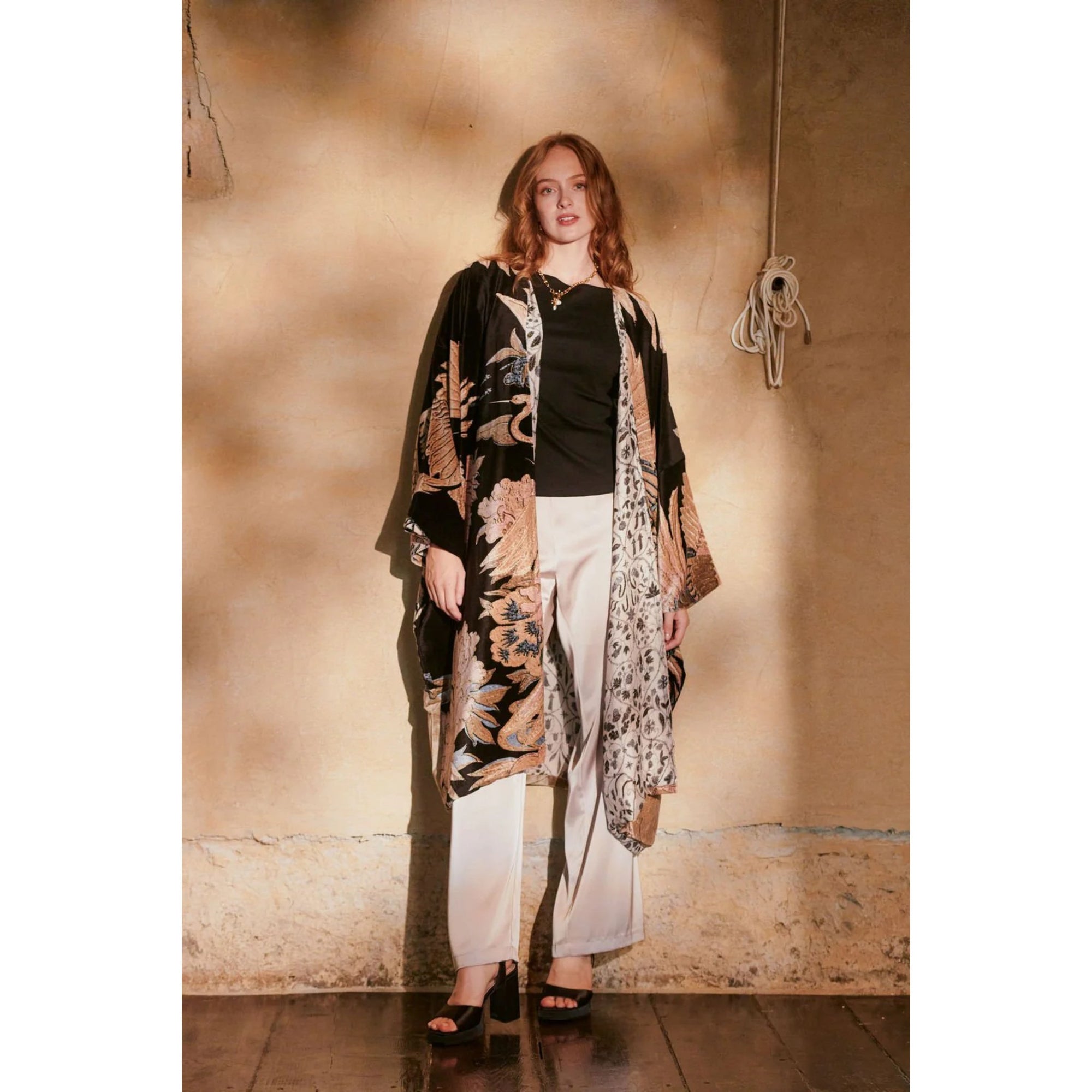 Woman wearing a patterned kimono-style garment against a textured wall.