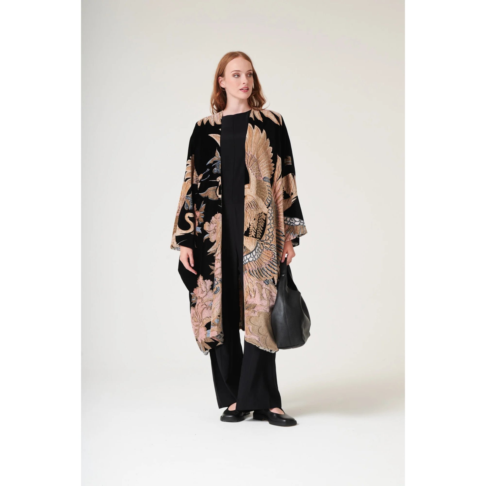 Woman wearing a long, patterned kimono over a black outfit on a white background