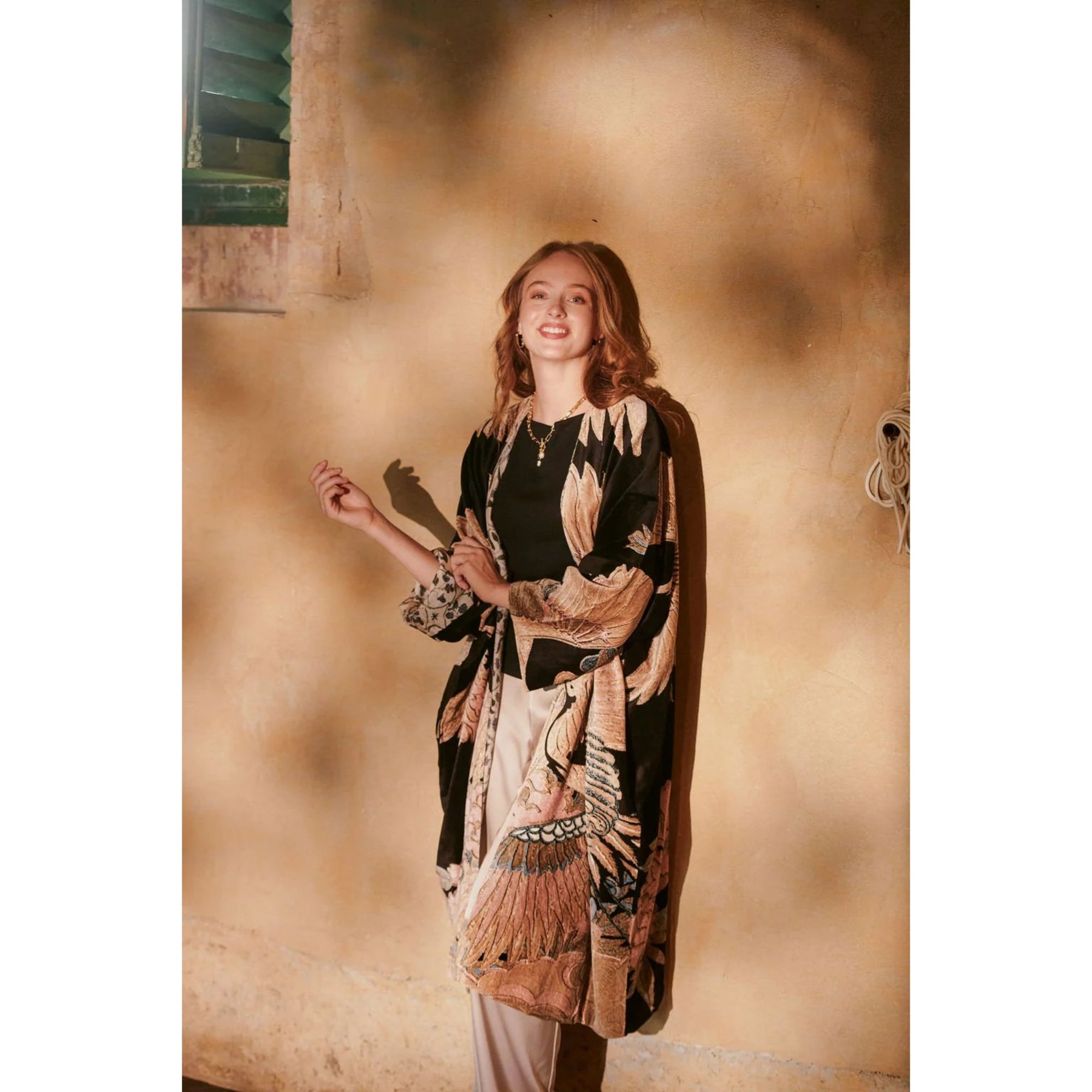 Woman wearing a long, patterned dress against a textured beige wall.