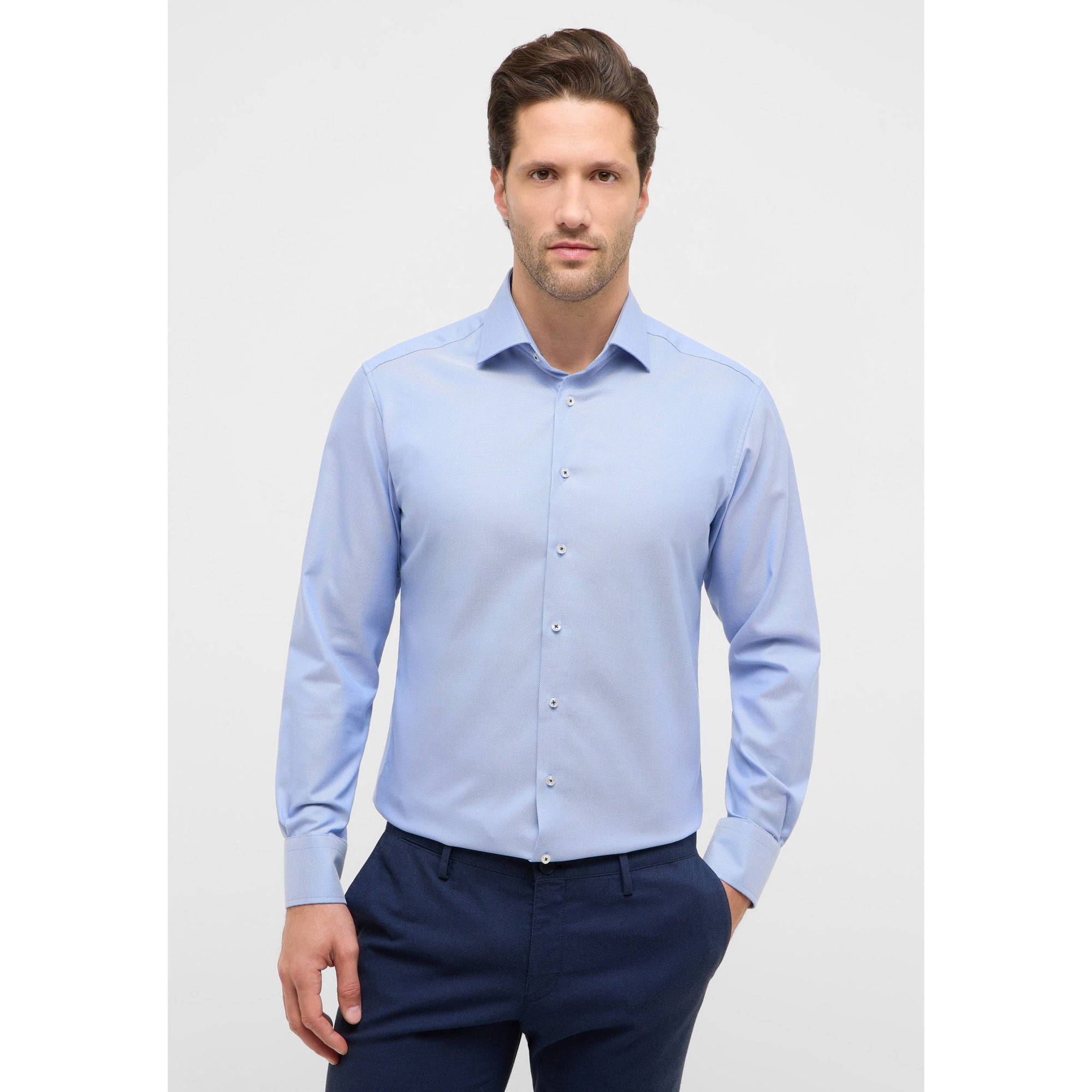 Man wearing a light blue dress shirt and dark blue pants on a white background