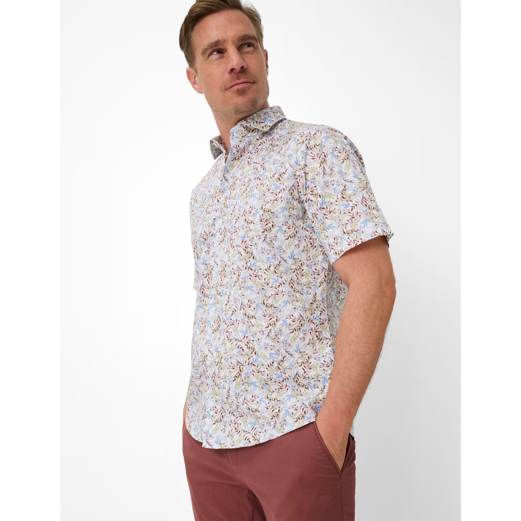 Man wearing a floral short-sleeve shirt and brown pants on a white background