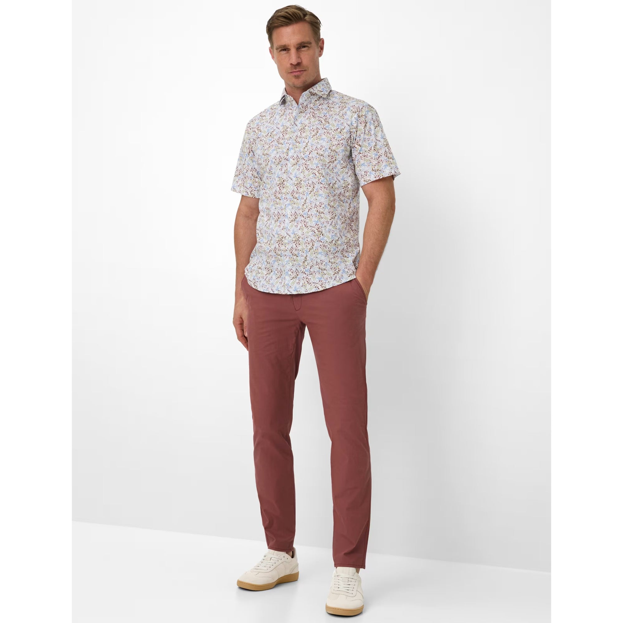Man wearing a patterned shirt and maroon pants on a white background