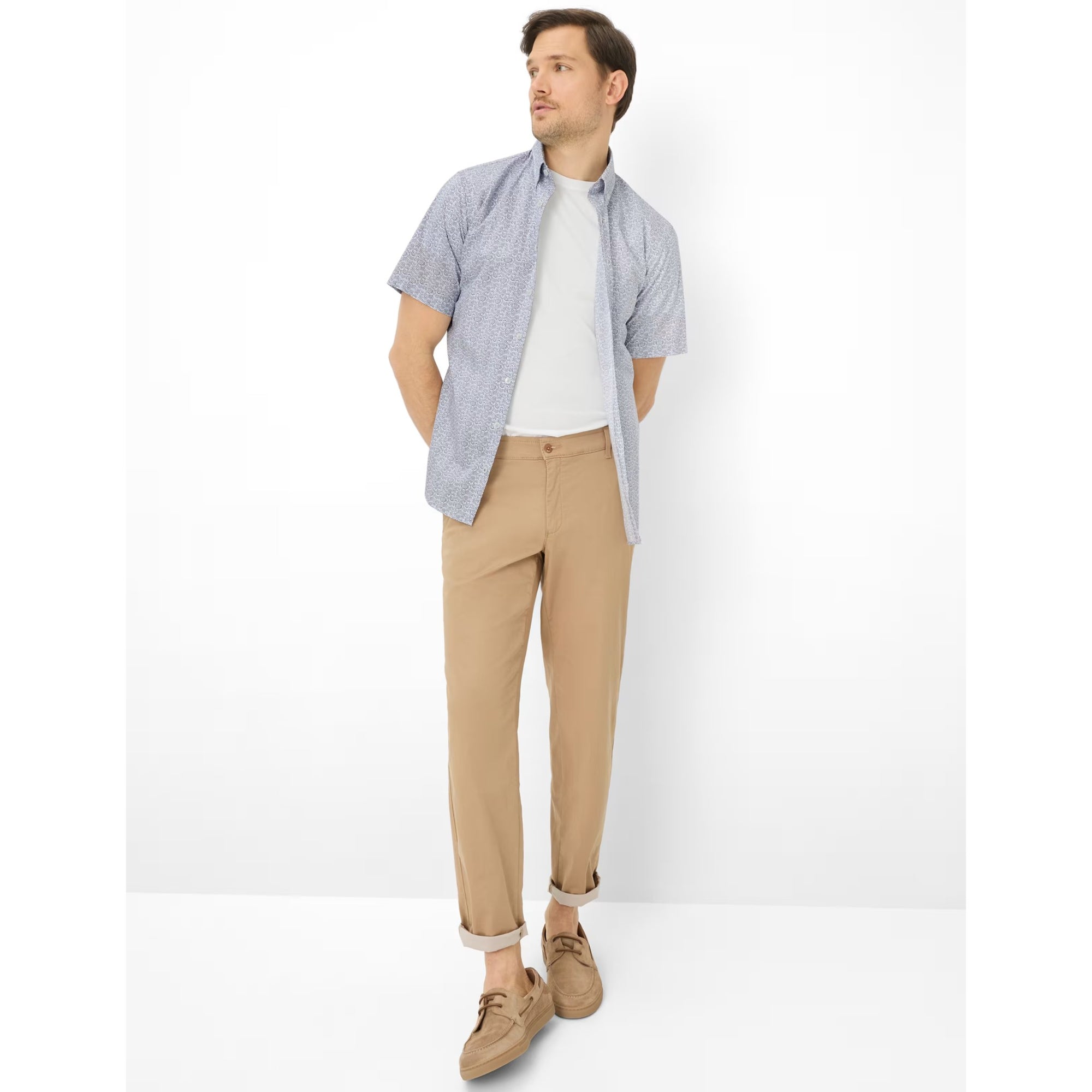 Man wearing a light blue checkered shirt, white t-shirt, beige pants, and brown shoes on a white background