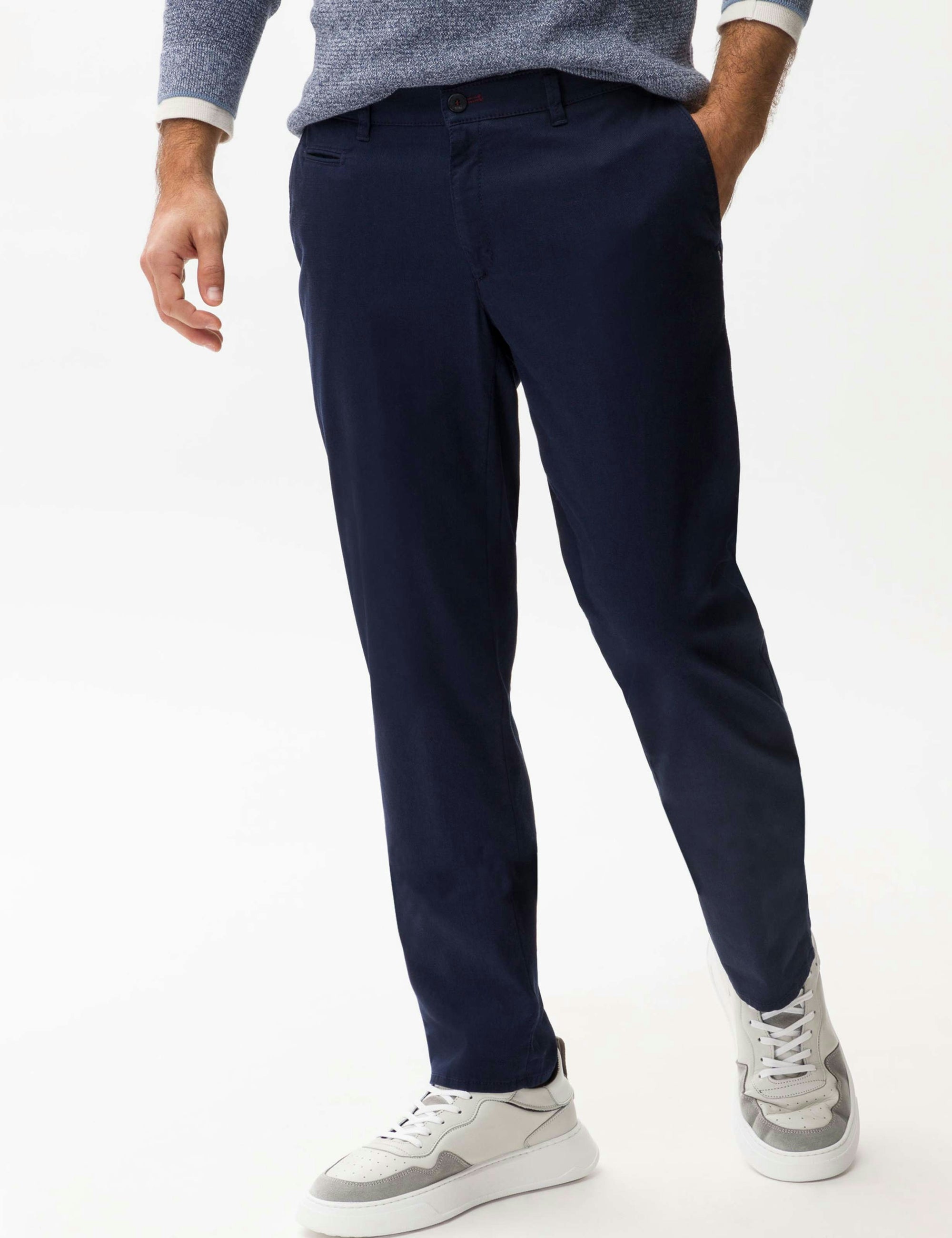 Person wearing navy pants and white sneakers on a white background