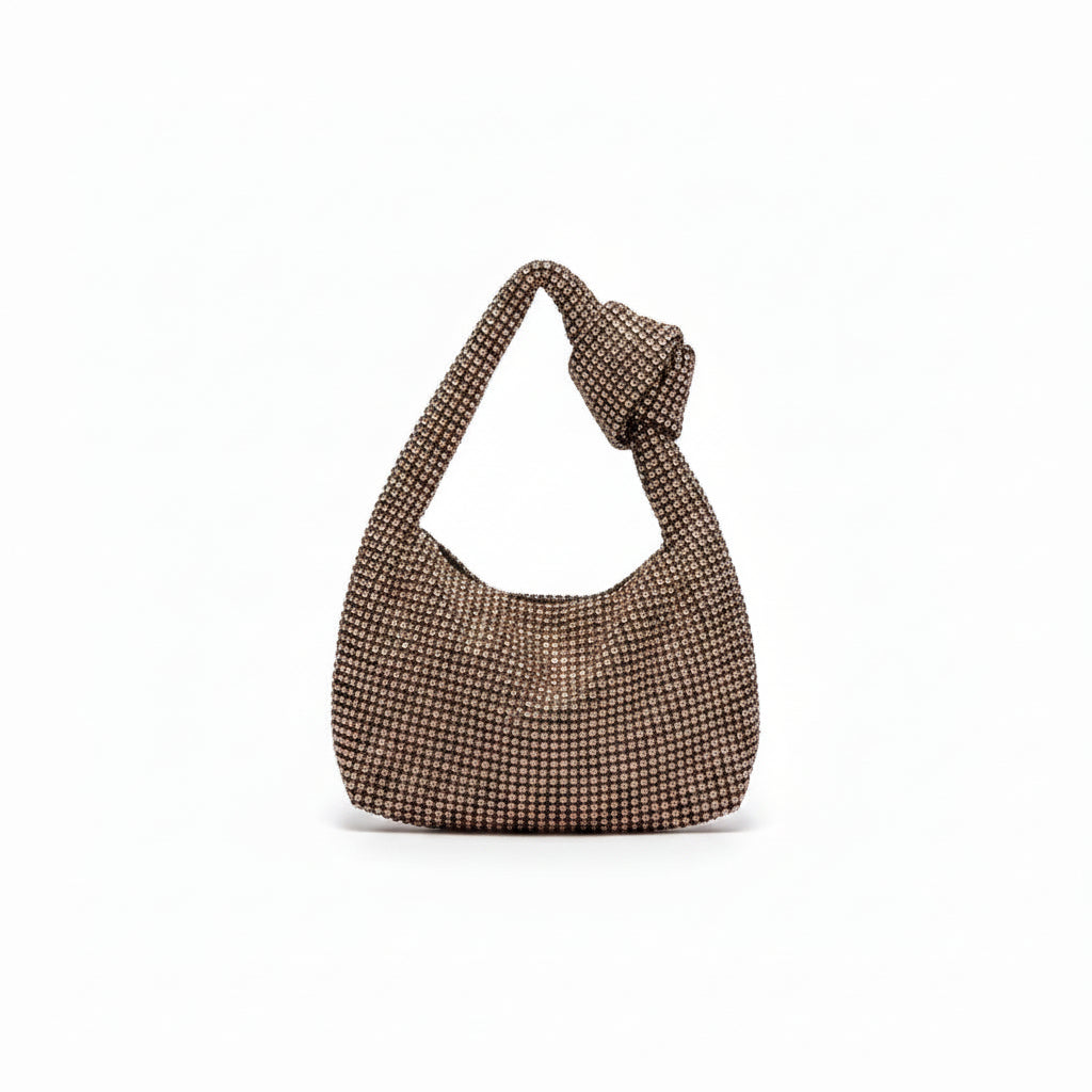 A slouchy shoulder bag covered in shimmering rhinestones, hanging from a metal hook against a white ribbed wall.