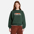 A model wearing a dark forest green Timberland crewneck sweatshirt with a 'TUMBLERLAND' graphic on the chest, paired with brown corduroy pants, against a light gray background.