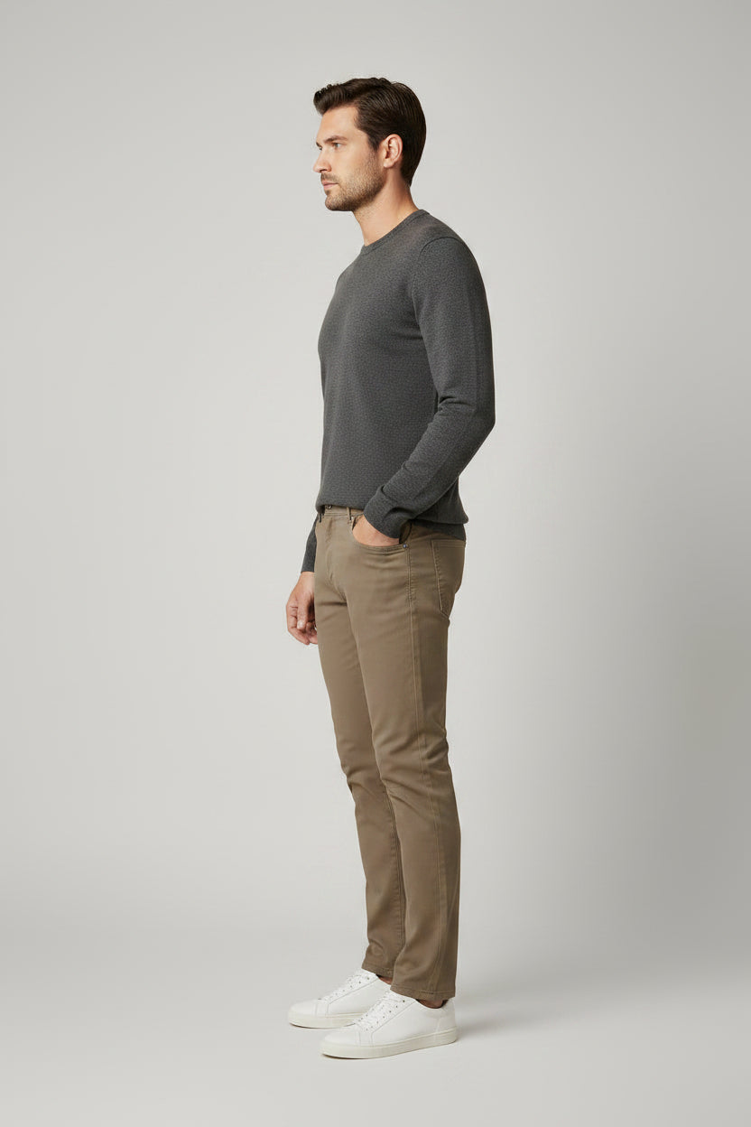 A man modeling a dark gray long-sleeve crewneck sweater, Brax tan slim-fit jeans, and white sneakers against a light gray studio background.