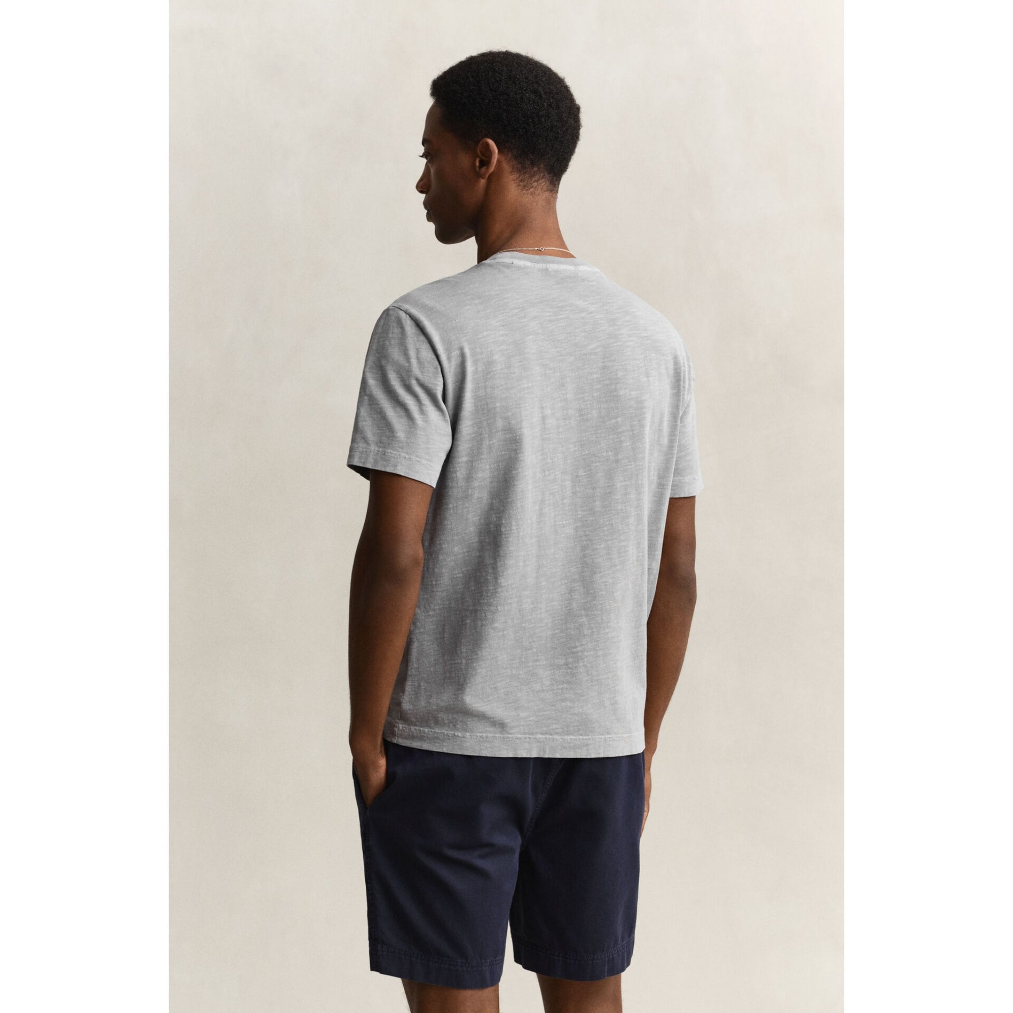 Man wearing a gray t-shirt and navy shorts on a beige background