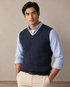 A man wearing a navy cable knit slipover with a light blue shirt and cream chinos