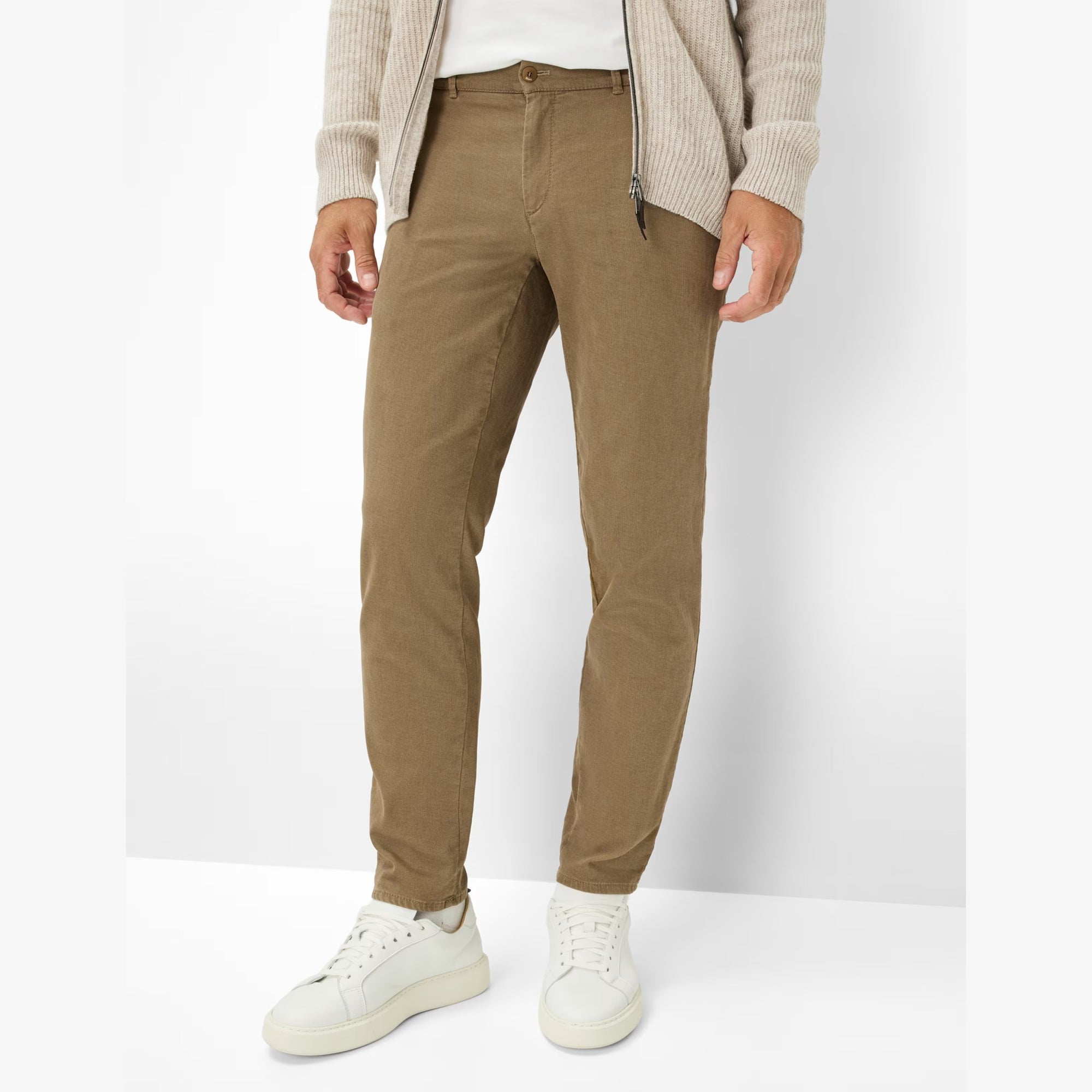 Person wearing Brax brown pants and white sneakers on a white background