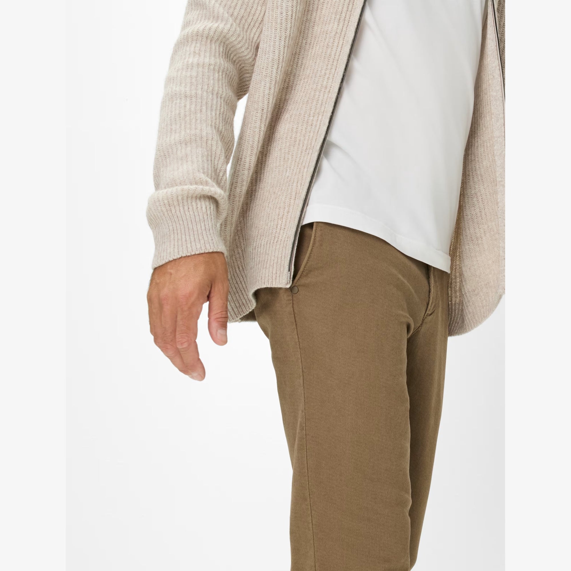 Person wearing a beige cardigan, white shirt, and brown pants on a white background