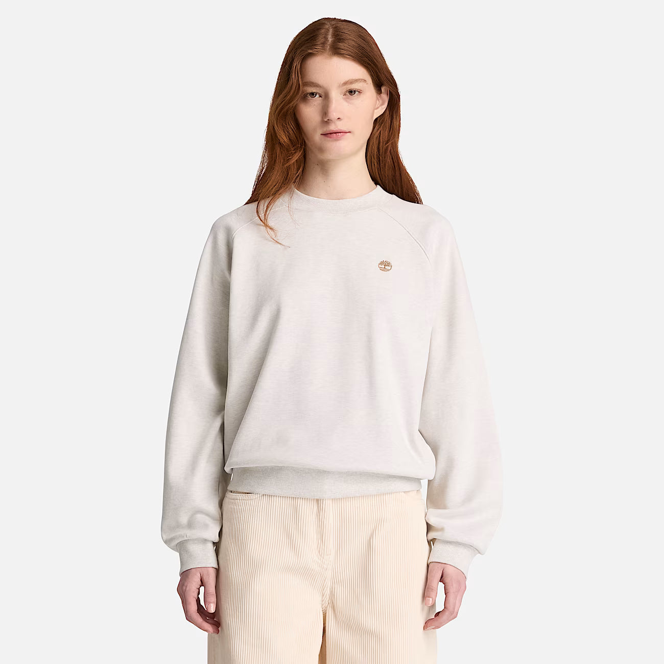A model wearing a Timberland  light beige crewneck sweatshirt with a small embroidered logo on the chest, paired with light beige corduroy pants, against a solid light gray background.