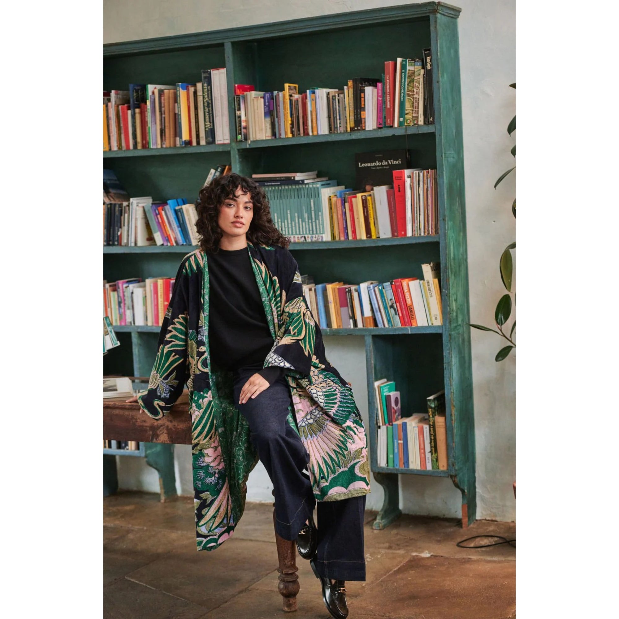 Woman in a patterned coat standing in front of a bookshelf filled with books.