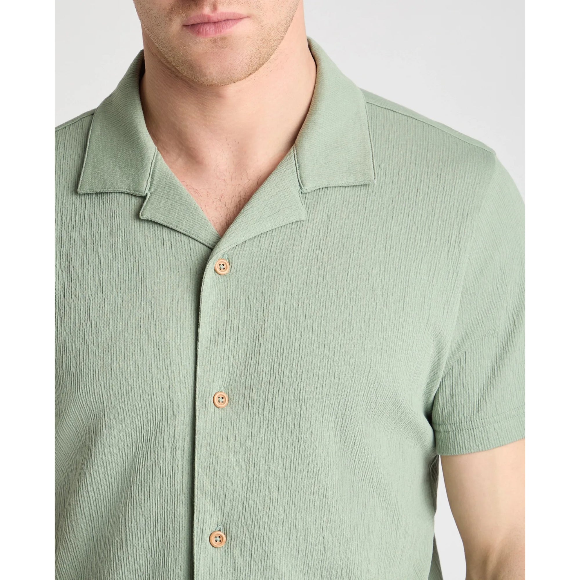 Green short-sleeve shirt with wooden buttons on a plain background