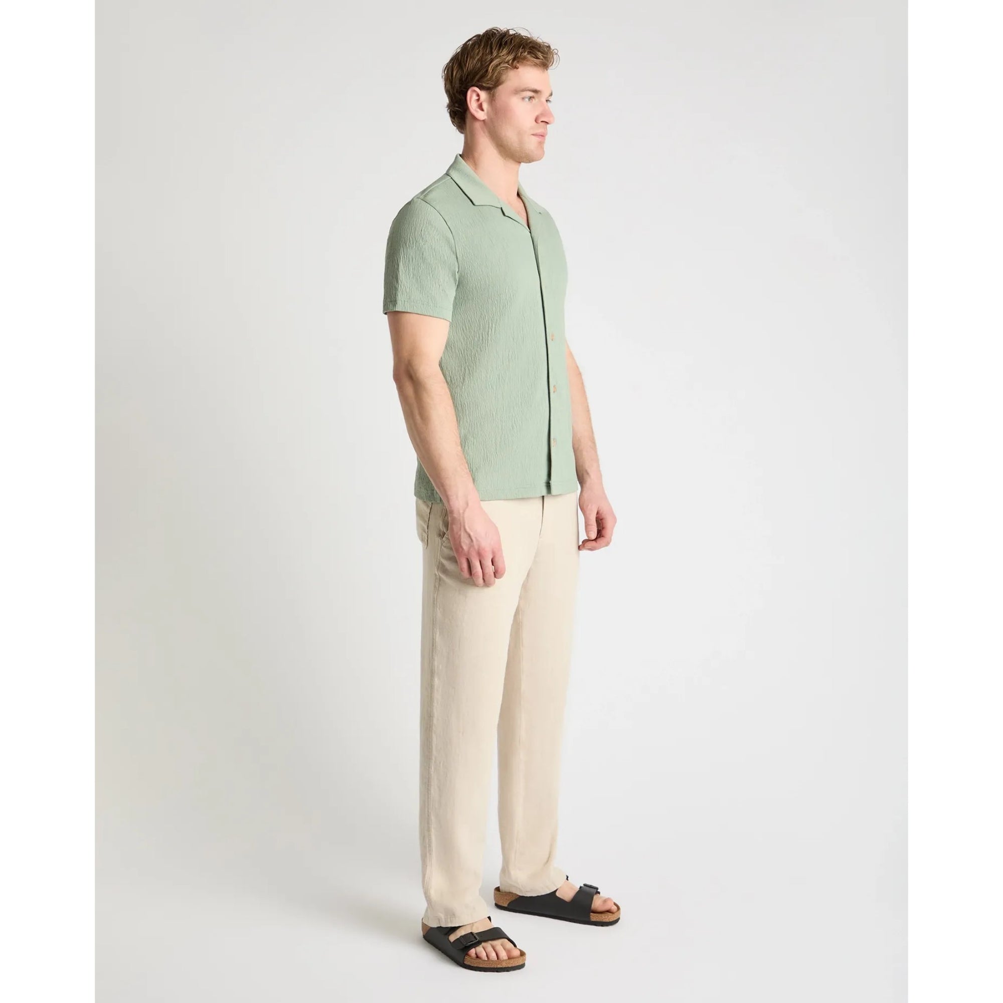 Man wearing a green shirt and beige pants on a white background
