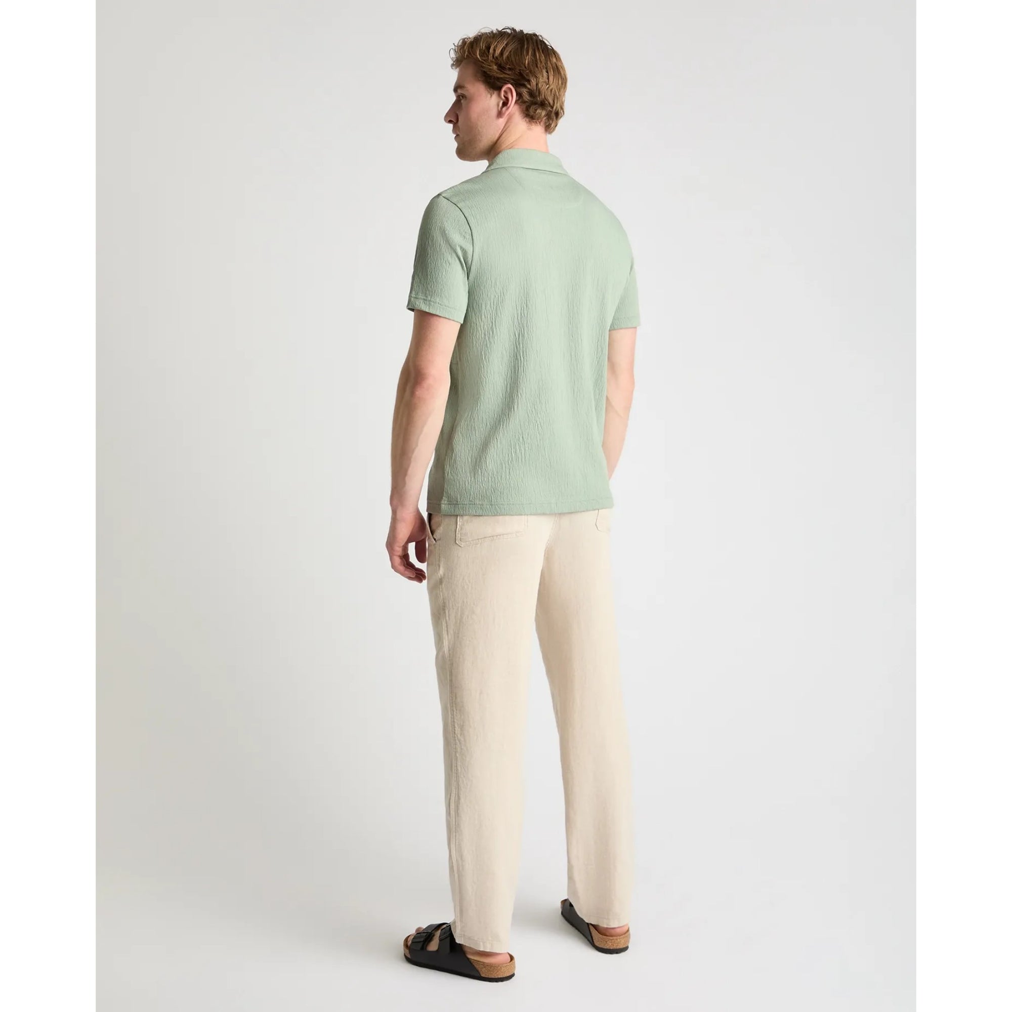 Man wearing a light green polo shirt and beige pants on a white background