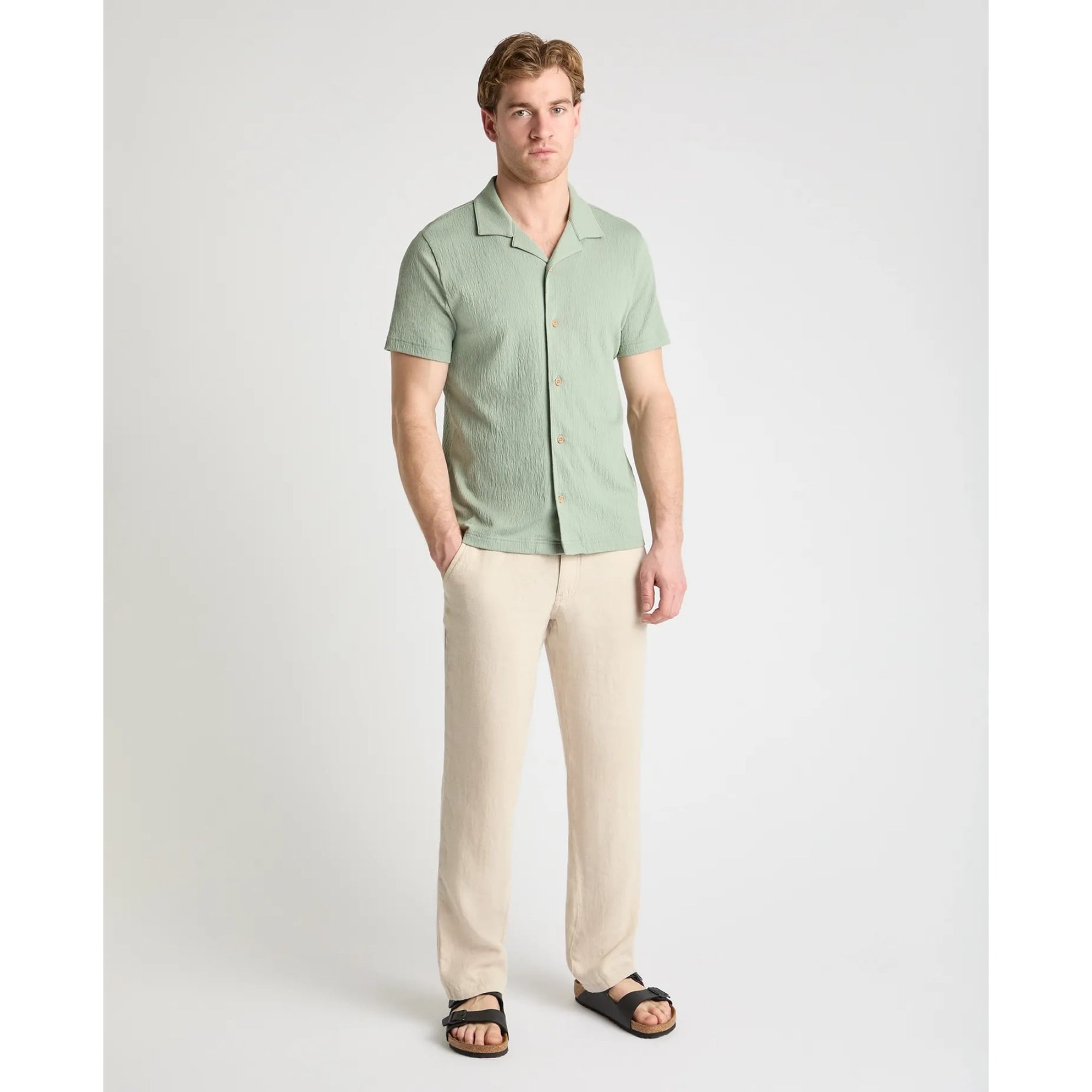 Man wearing a light green shirt and beige pants on a white background
