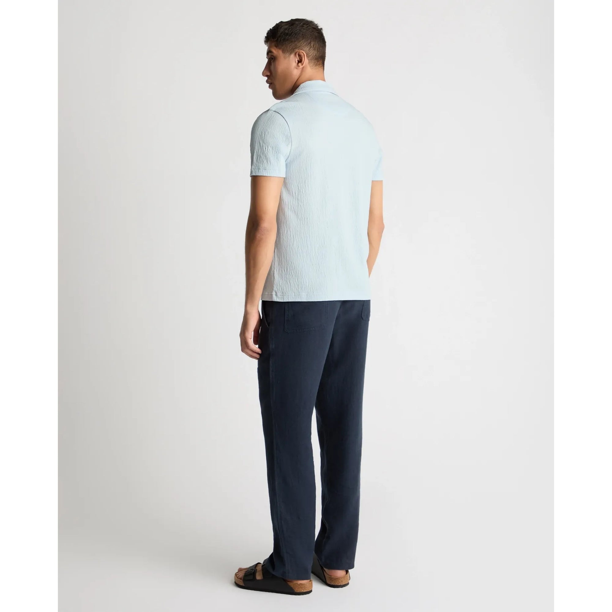 Man wearing a light blue striped polo shirt and dark blue pants on a white background