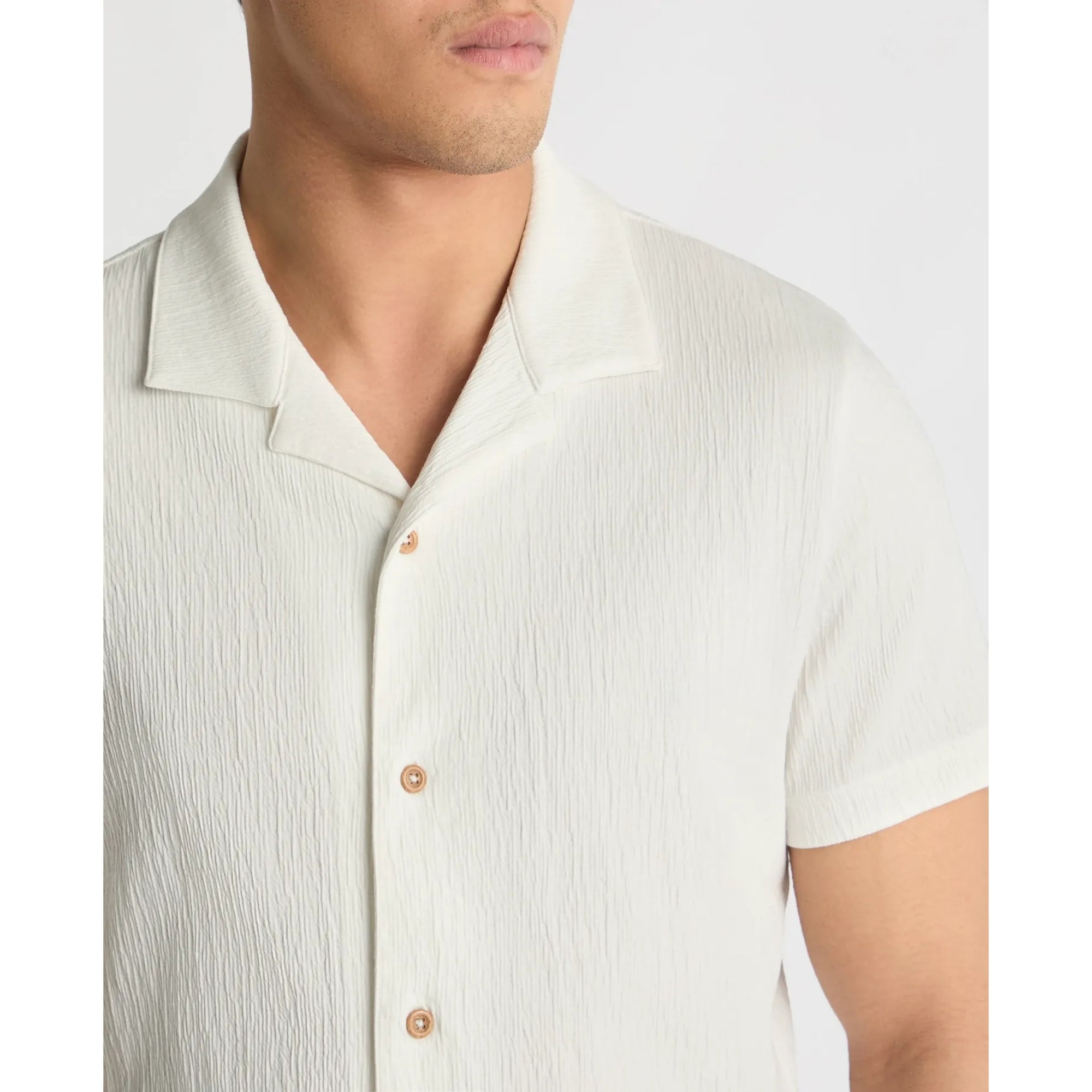 Close-up of a person wearing a light-colored short-sleeve shirt with buttons on a plain background