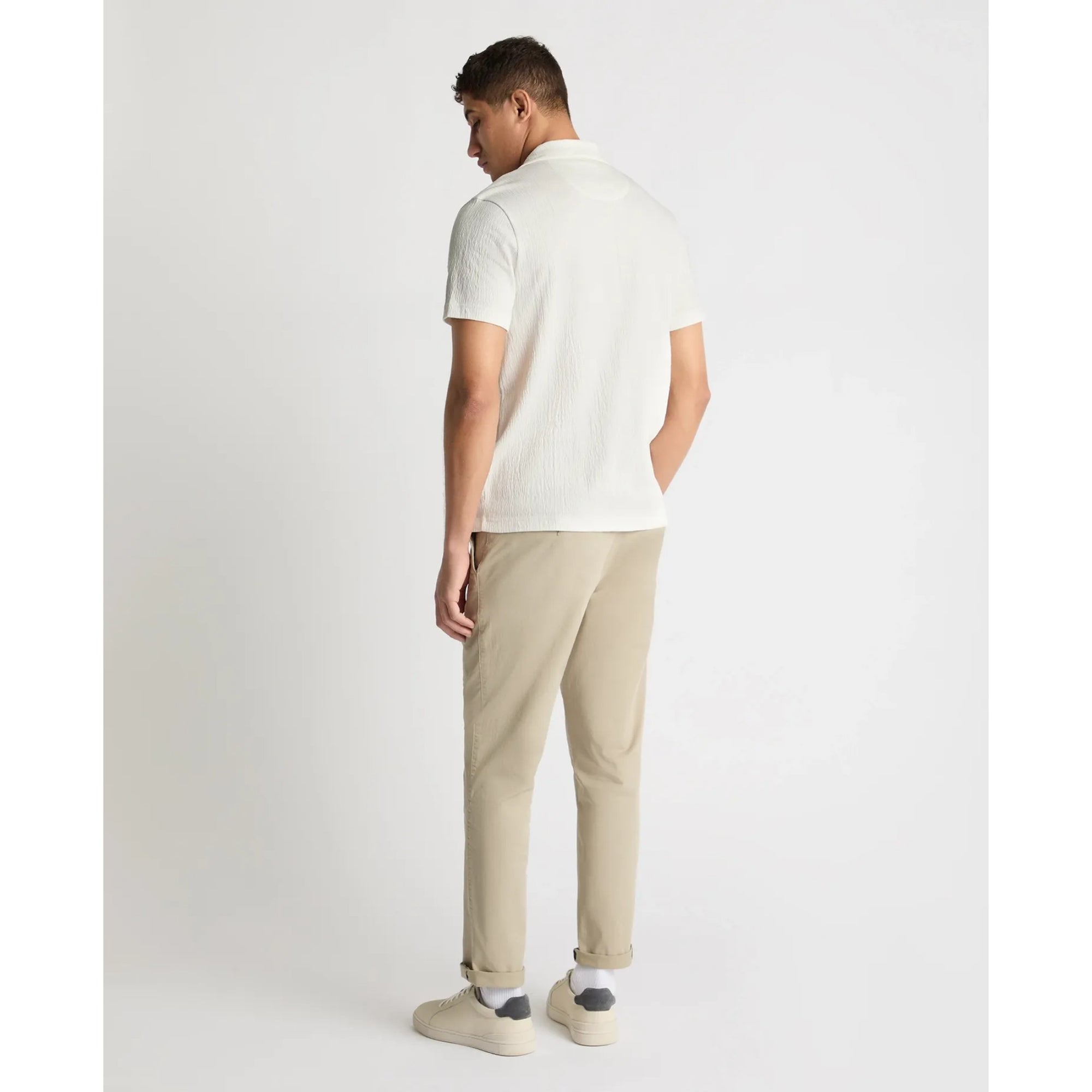 Man wearing a white polo shirt and beige pants on a white background